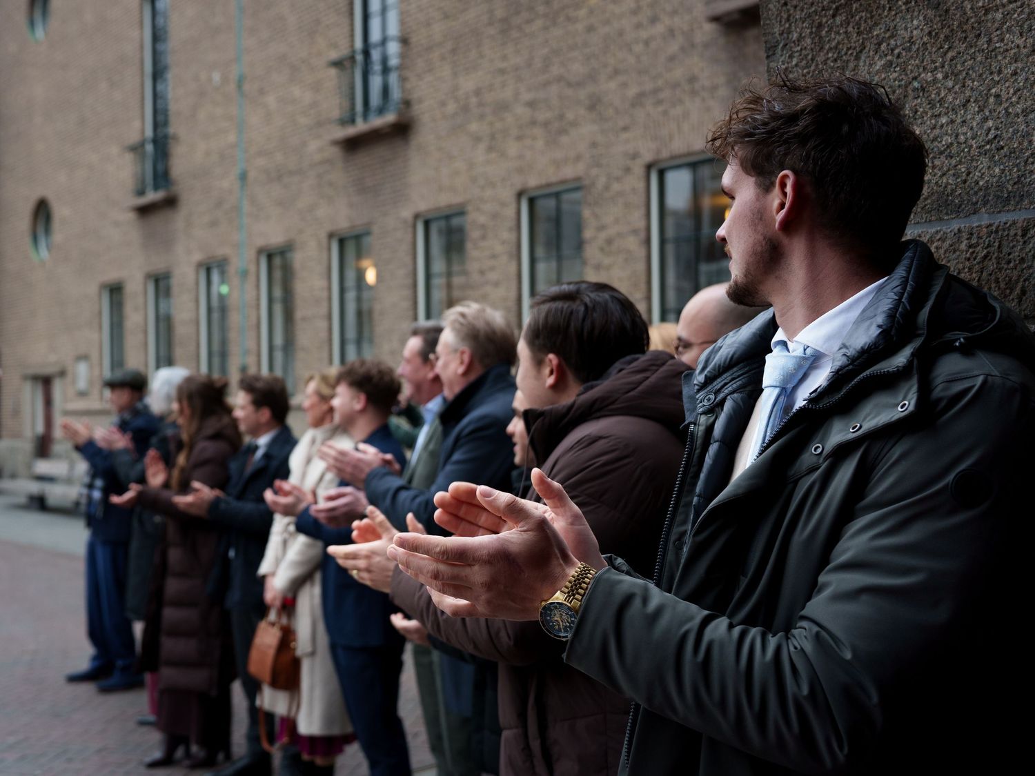 Group of people clapping and applauding in a line outside a brick building during a formal outdoor gathering.