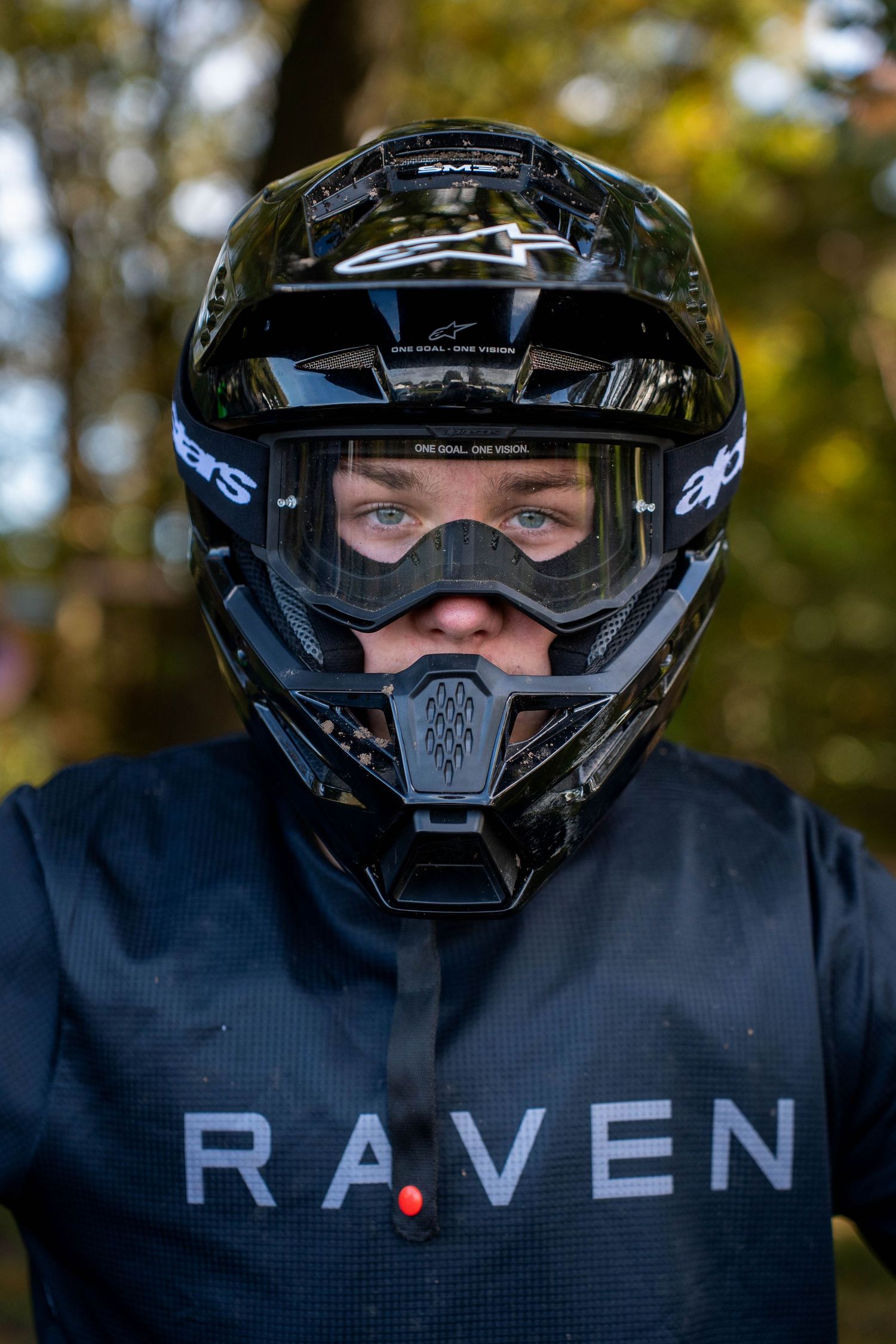 Person wearing a black Alpinestars motocross helmet with goggles and a Raven jersey, photographed outdoors.