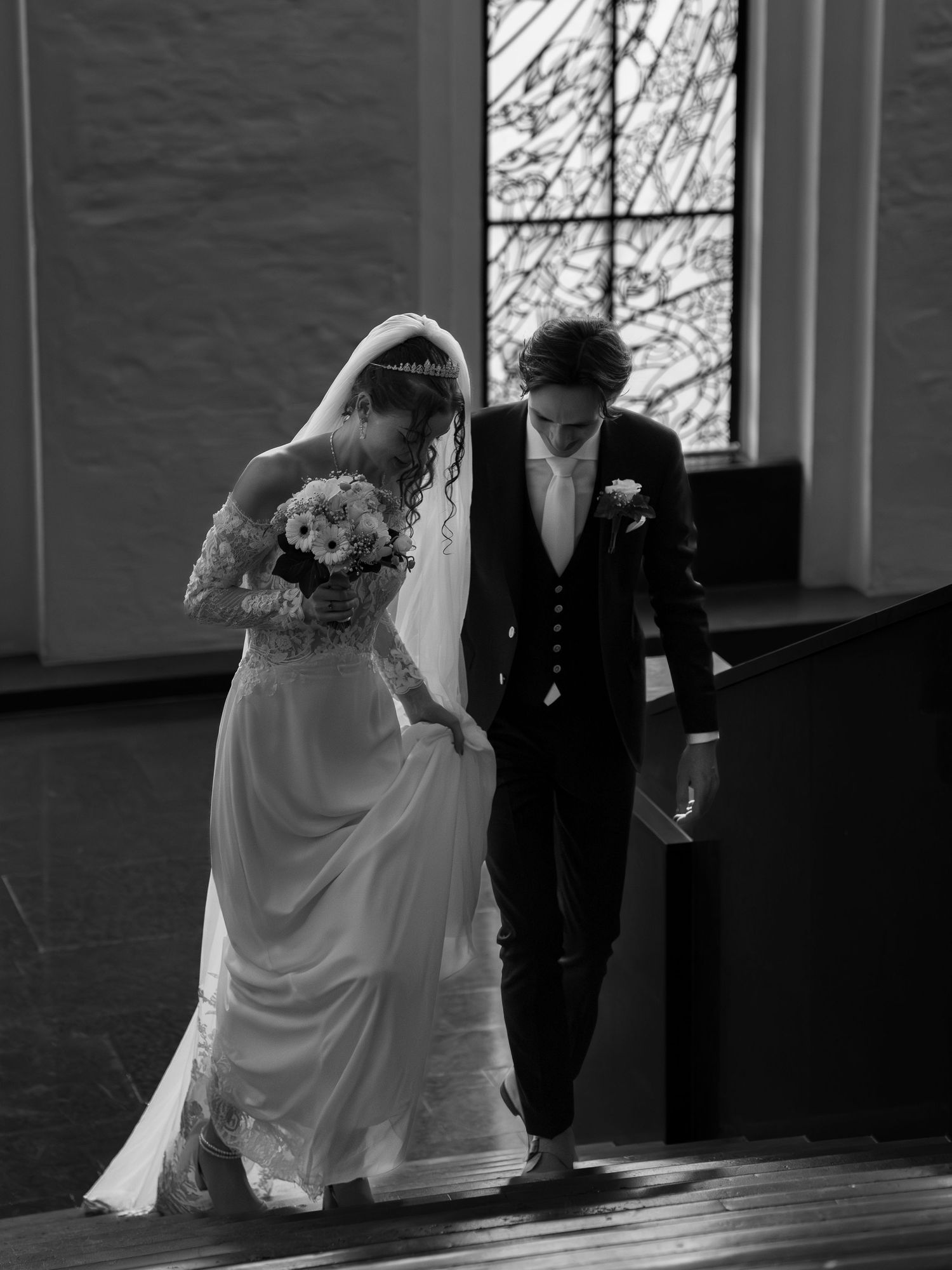 Black and white photo of a bride and groom walking together in a church, bride holding a bouquet.