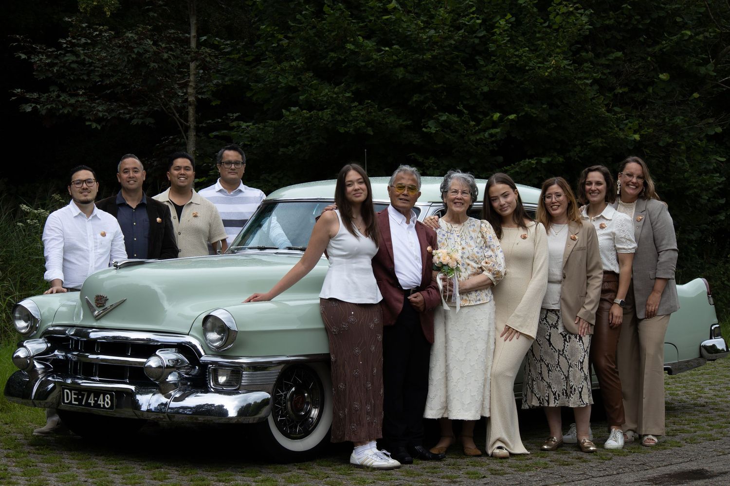 Family members arranged in formal poses with vintage cars on a grassy lawn.