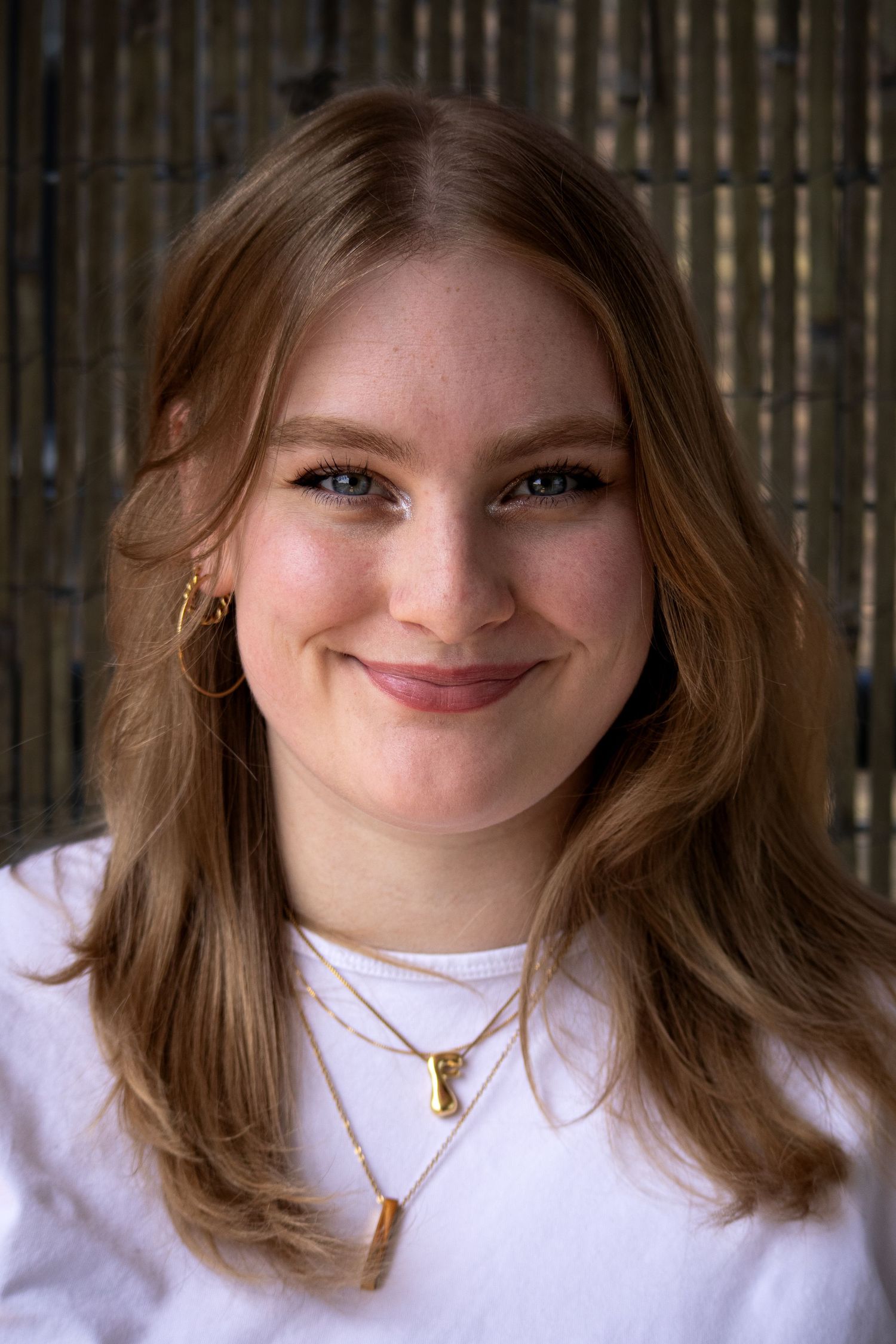 A person wearing a white shirt and gold necklace smiles in a close-up.
