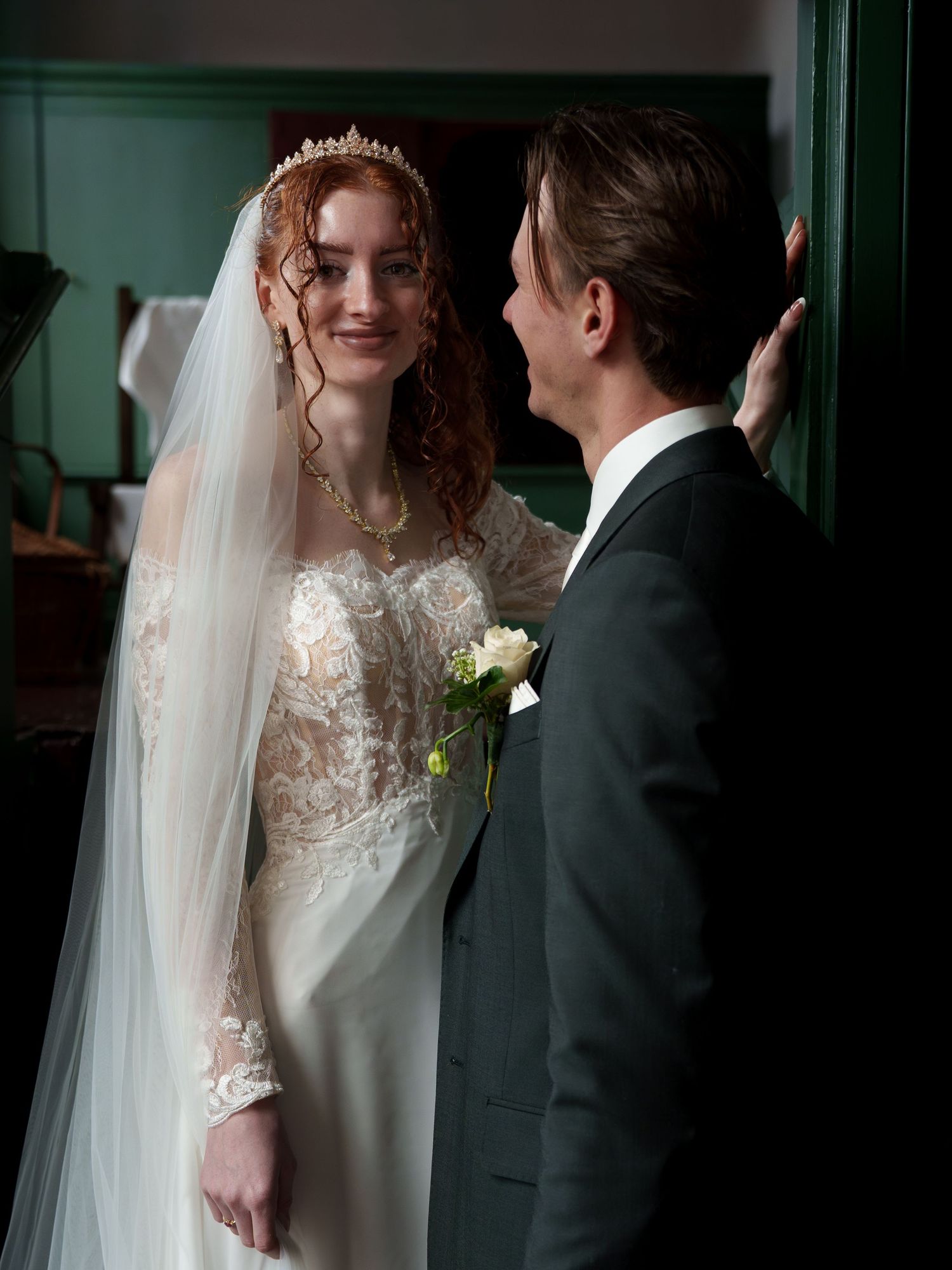 A bride in lace gown and tiara shares a tender moment with groom in dark suit at their wedding ceremony.