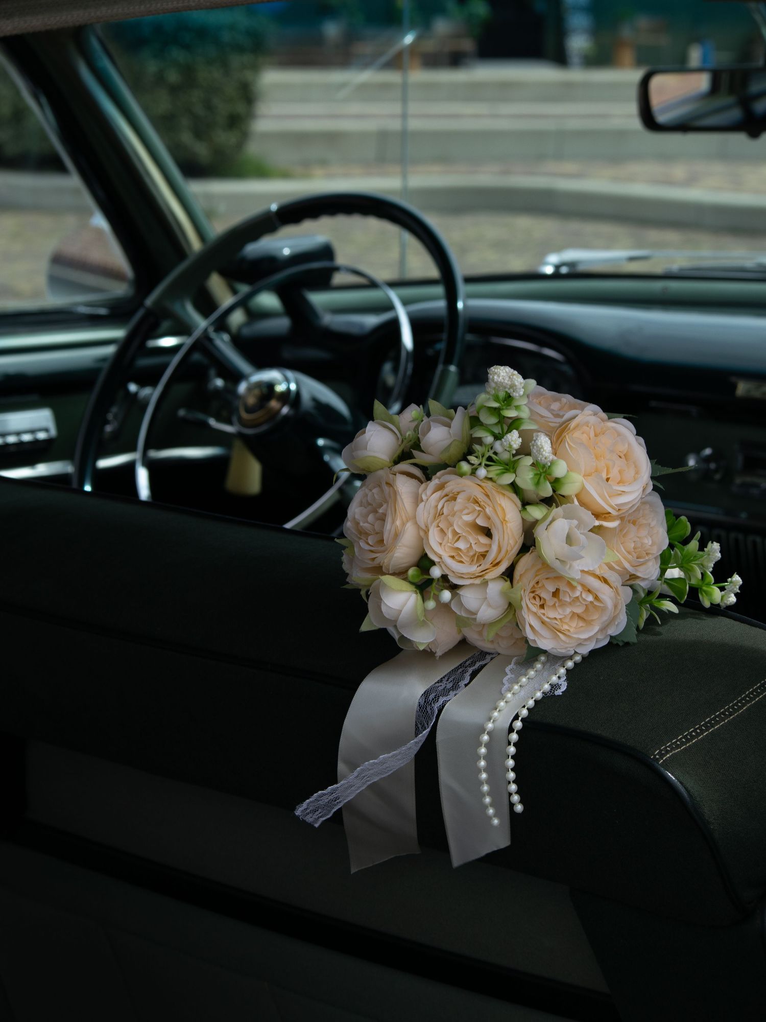 Elegant bridal bouquet of blush roses with pearl ribbon resting on vintage car dashboard.