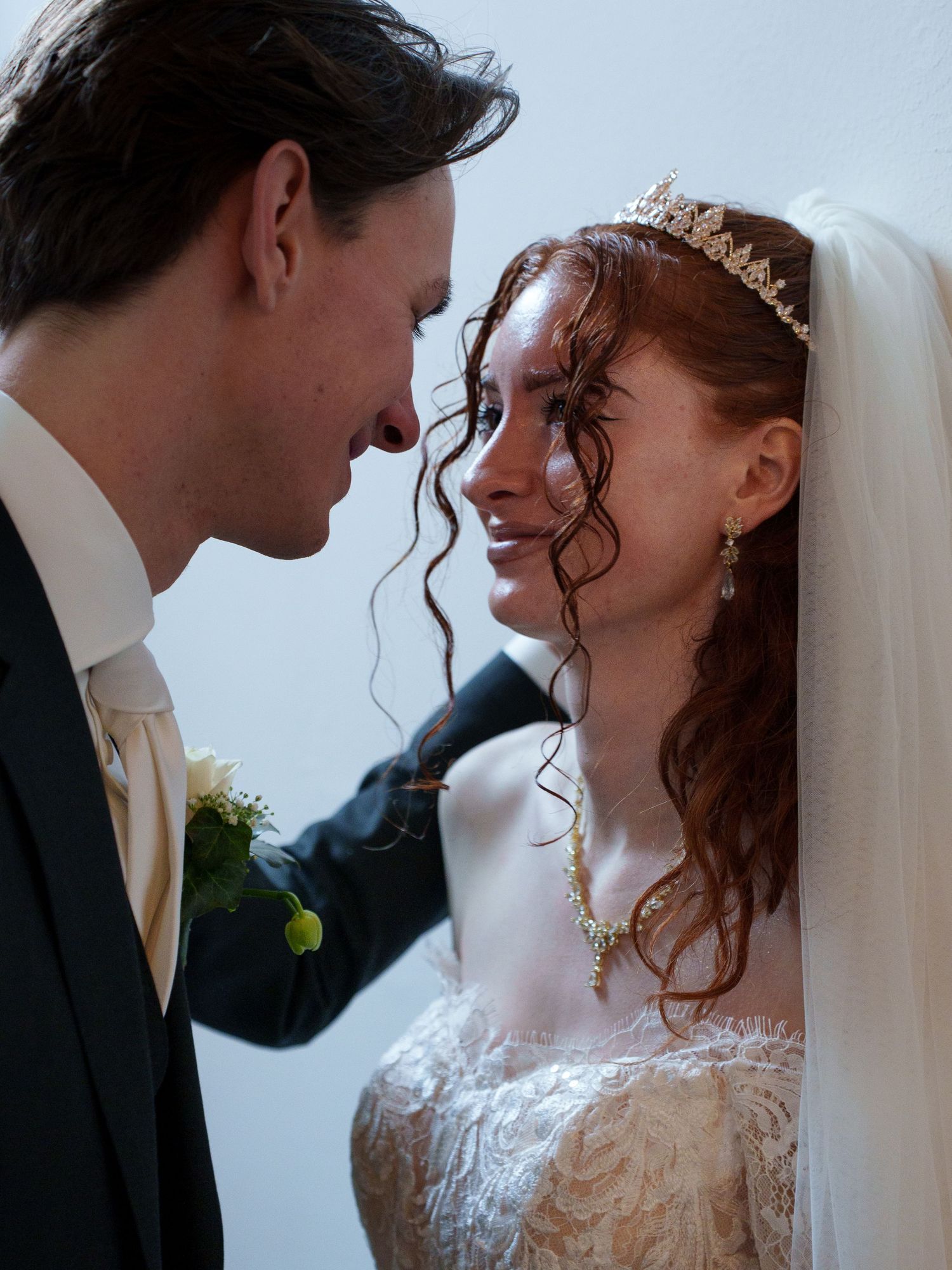 A bride wearing a tiara and groom in a suit share an intimate moment on their wedding day.