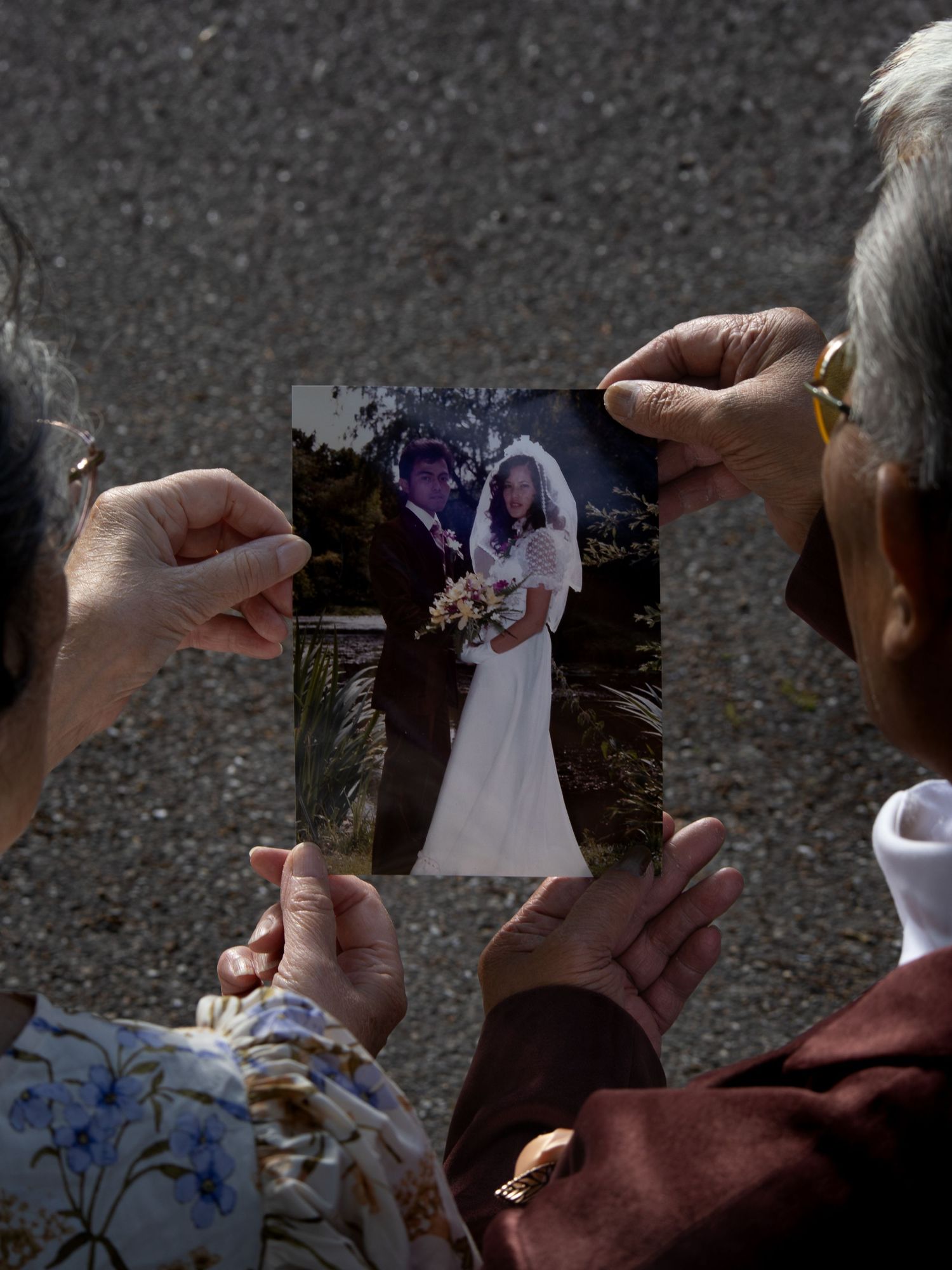 Two elderly people holding a wedding photo of a bride and groom, reminiscing about a special day outdoors.