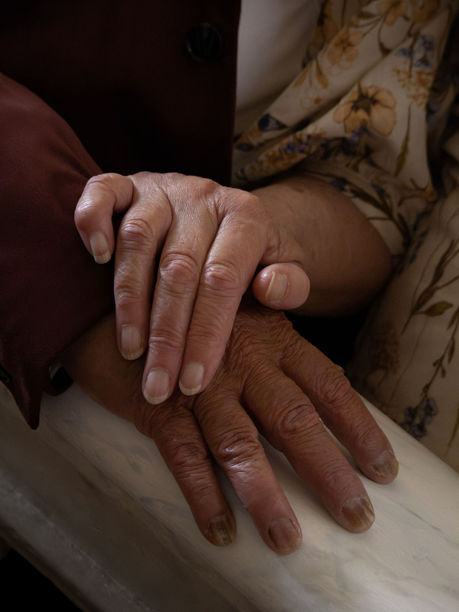 Close-up of two elderly people holding hands tenderly, showing aged skin and a floral garment.