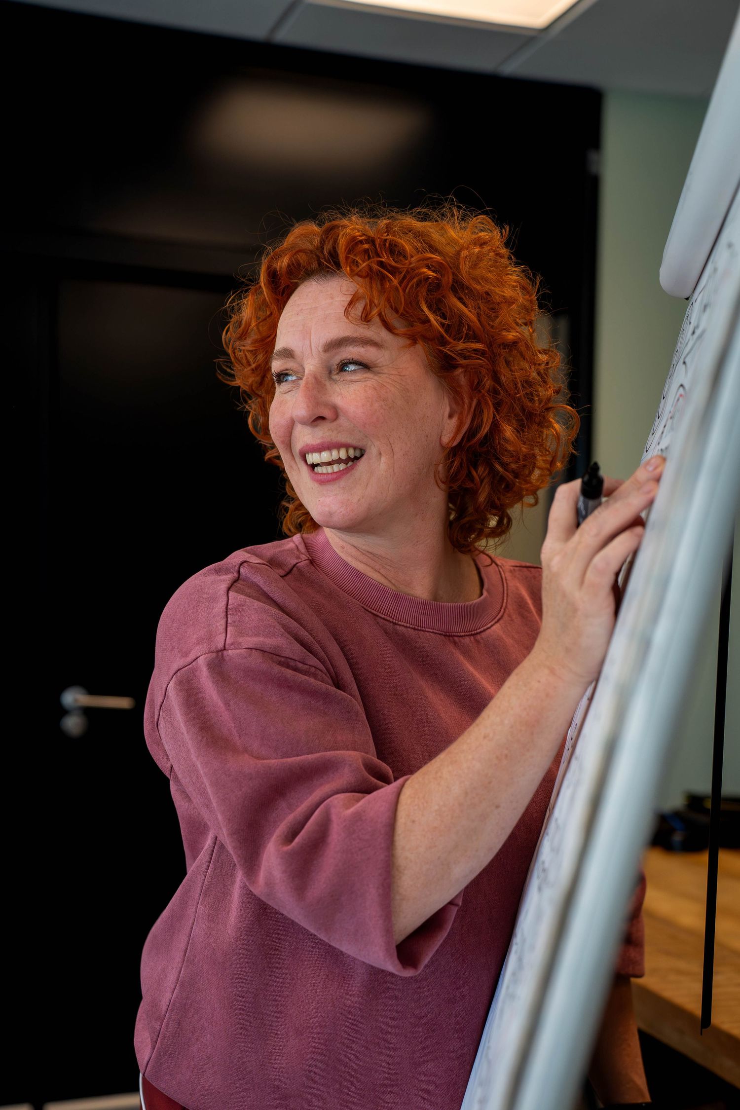 A person with vibrant red curly hair wearing a mauve shirt is shown in a sequence of candid expressions.