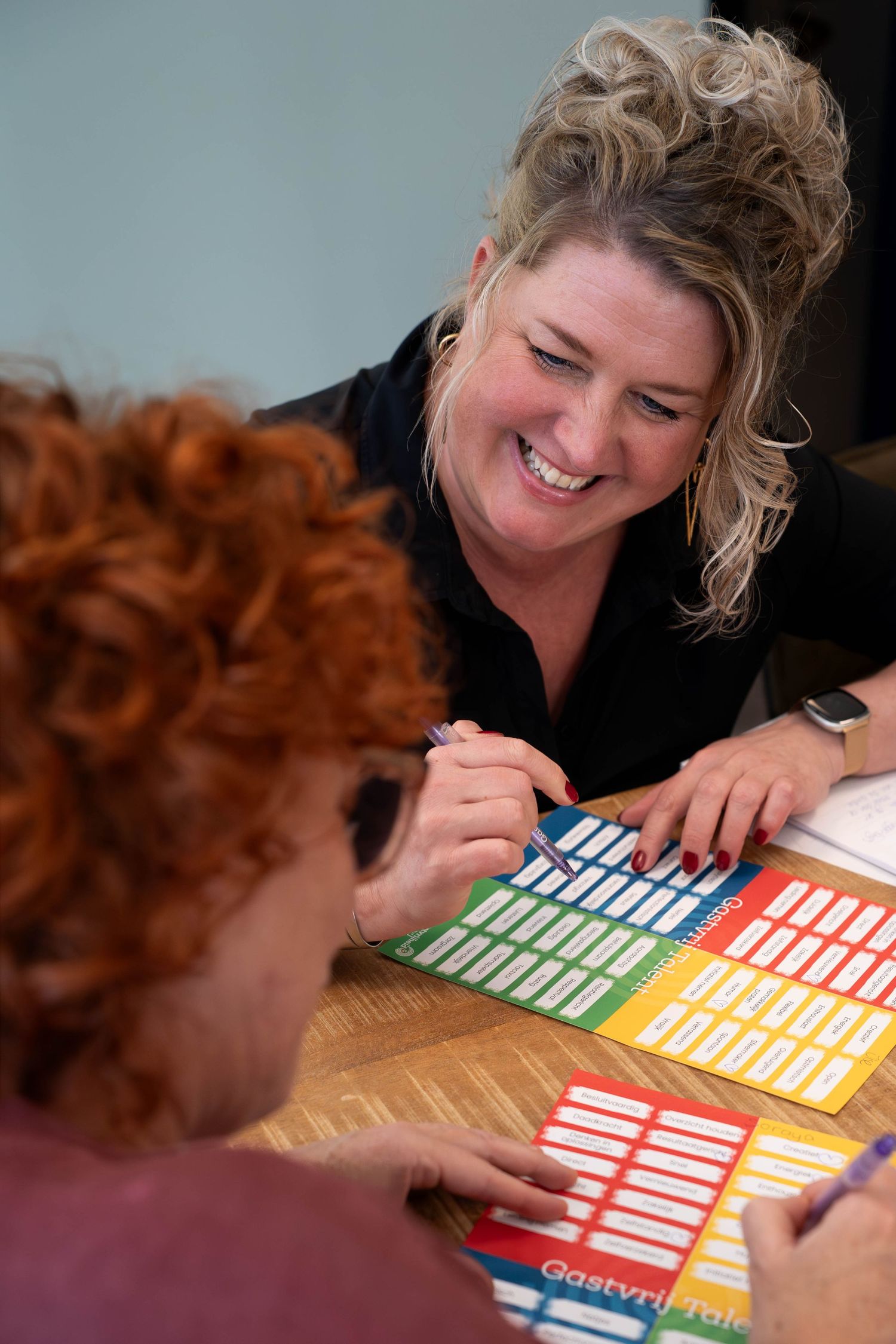 Two women smiling and reviewing colorful charts together at a wooden table in a collaborative meeting.