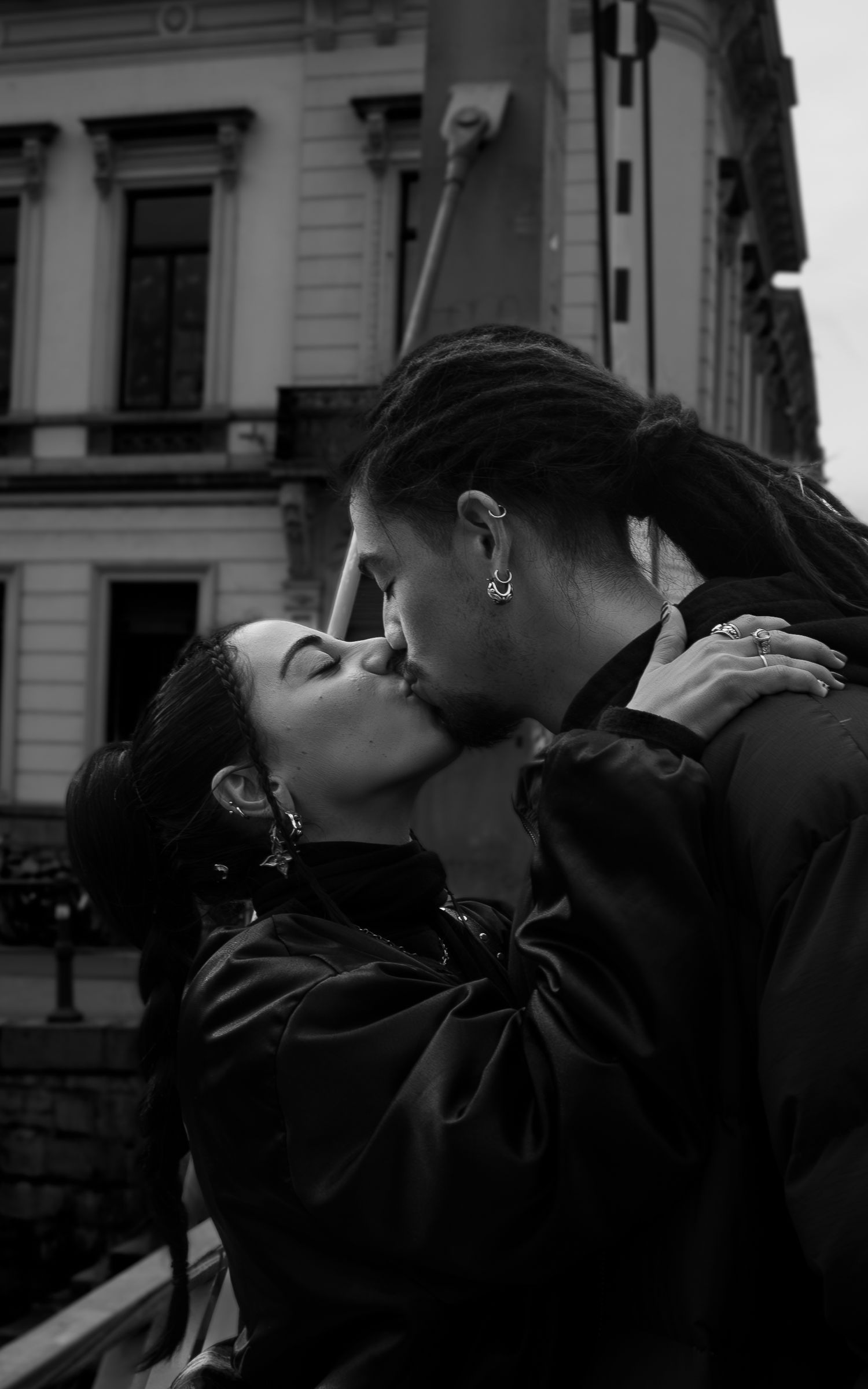 A romantic black and white photograph of a couple sharing a tender kiss on an urban street with historic buildings in background.