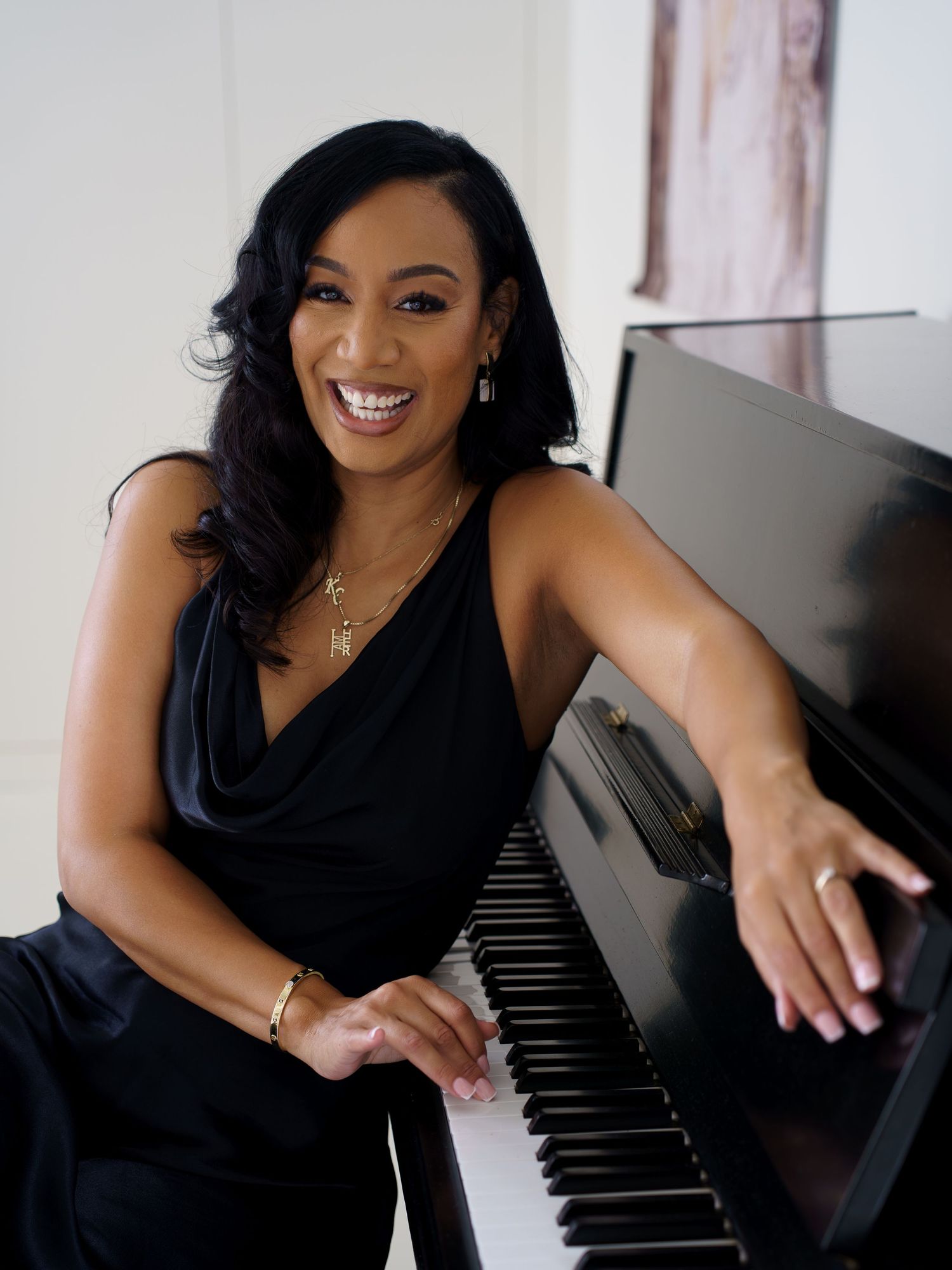Smiling woman in black dress posing at a piano, showcasing elegance and musical talent in a bright studio setting.