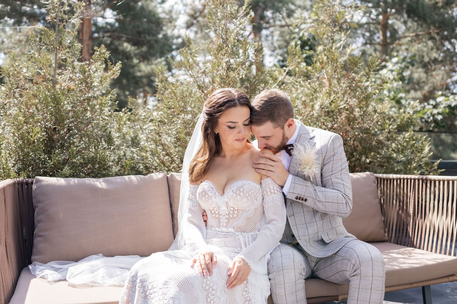 Wedding couple shares romantic moments on an outdoor bench surrounded by pine trees.