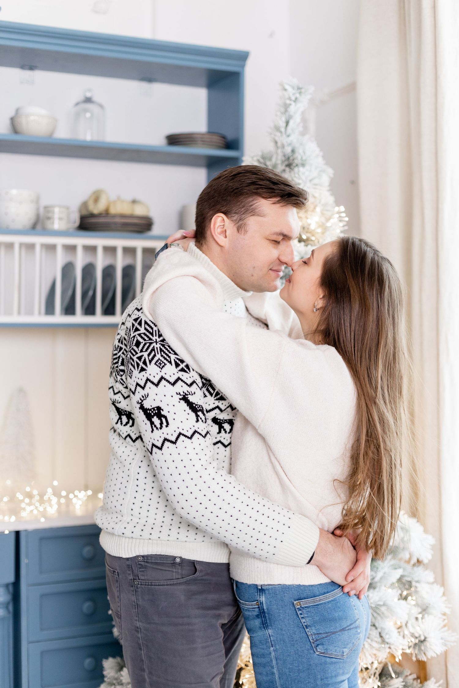 Romantic moment captured in front of blue built-in shelves with winter holiday decorations.