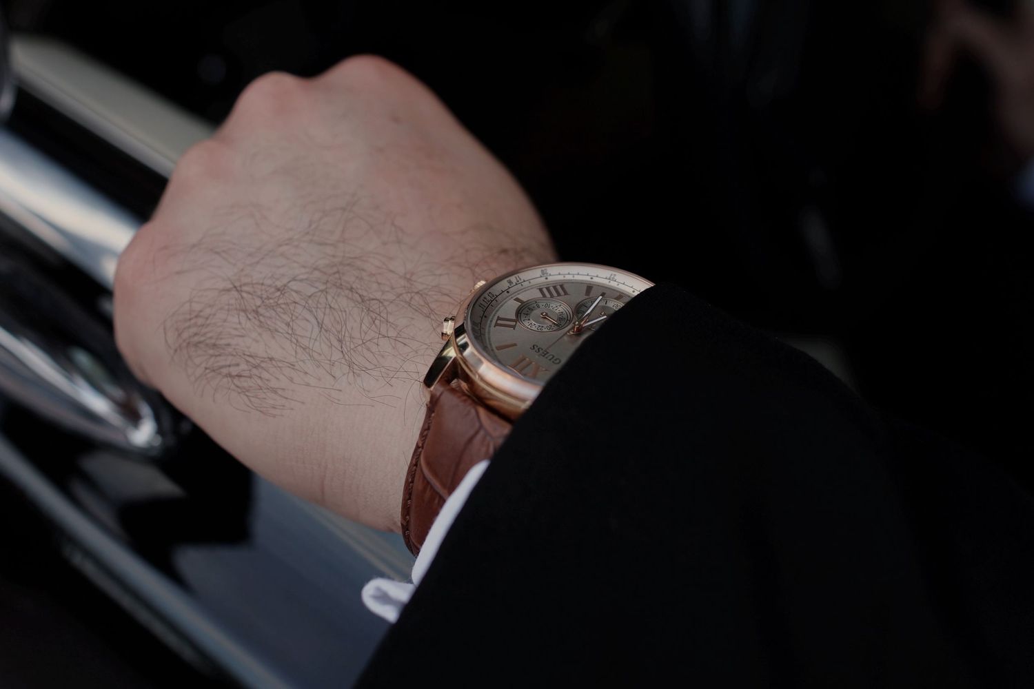 Close-up of a man wearing a luxury rose gold watch with brown leather strap on his wrist.