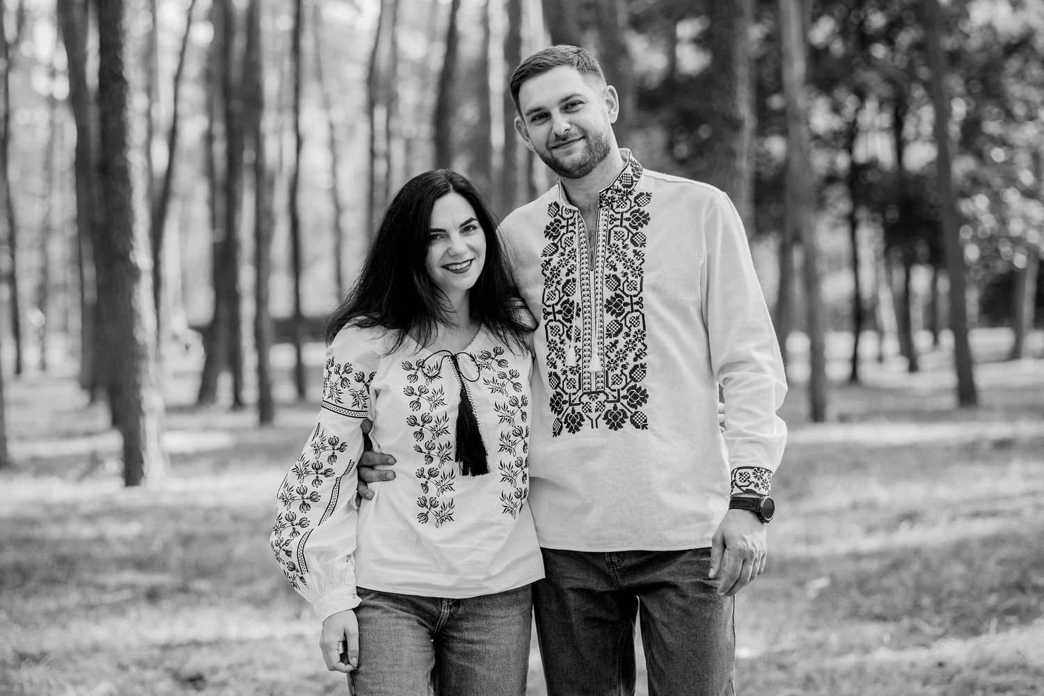 Couple in Ukrainian embroidered vyshyvanka shirts smiling together in a forest park, black and white photo.