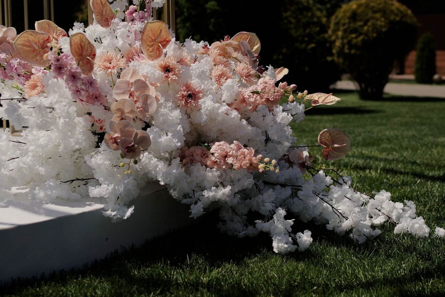 Elegant outdoor wedding floral arrangement with white and blush pink flowers cascading on green grass.