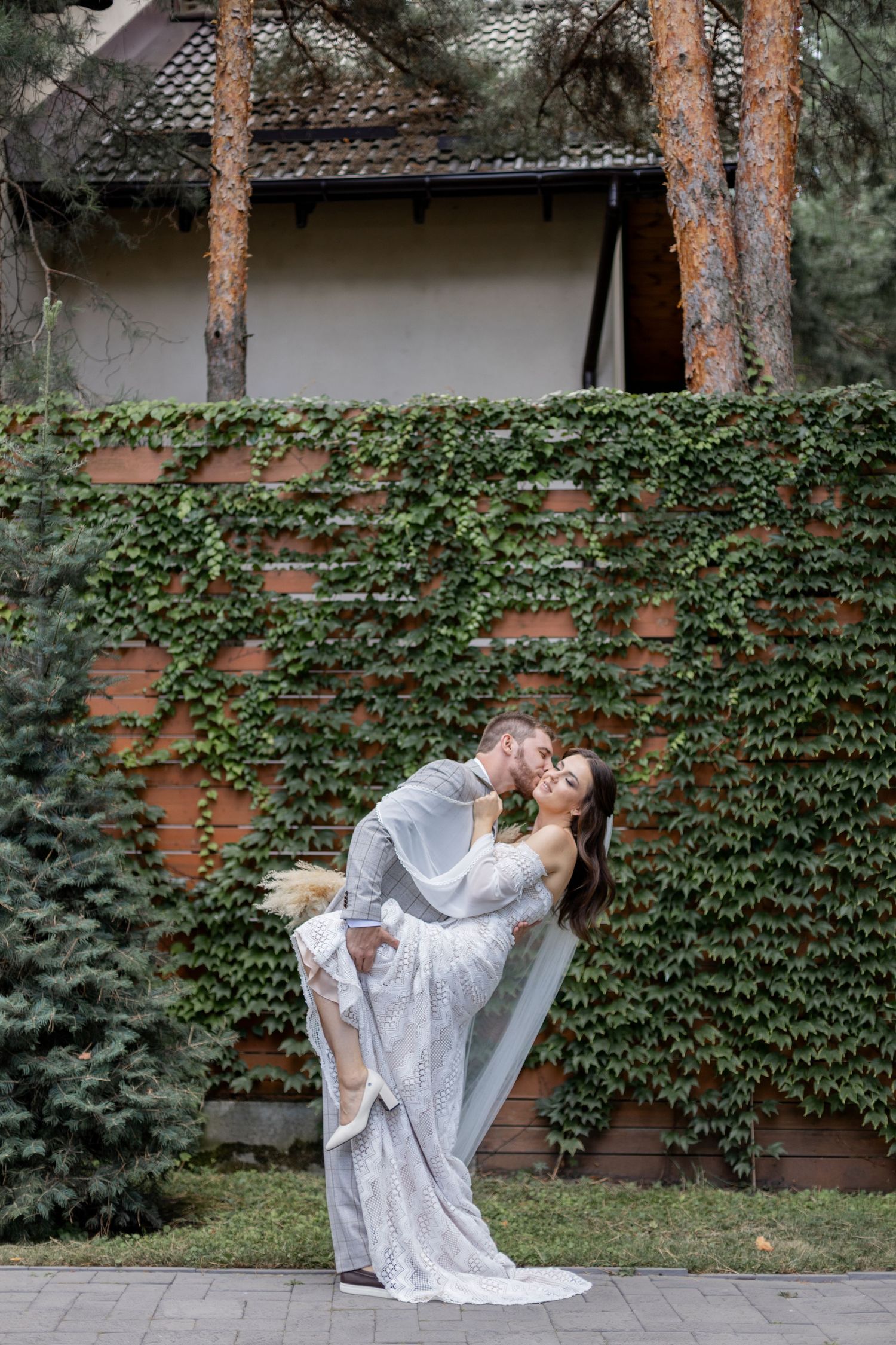 Romantic dip kiss pose against ivy-covered wall in garden setting.
