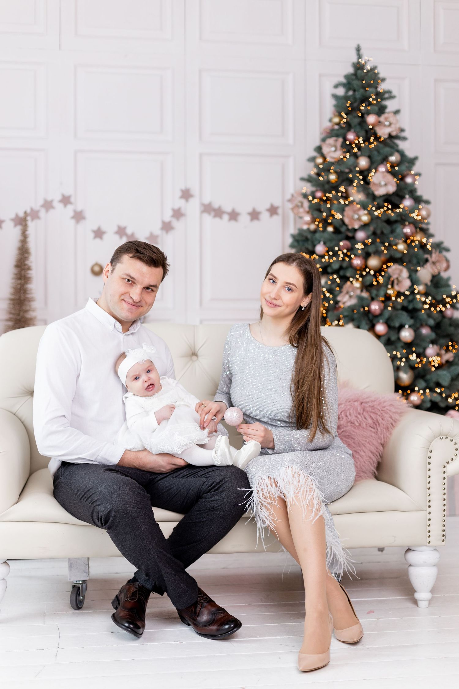 Family in coordinated outfits sitting on white couch by Christmas tree.