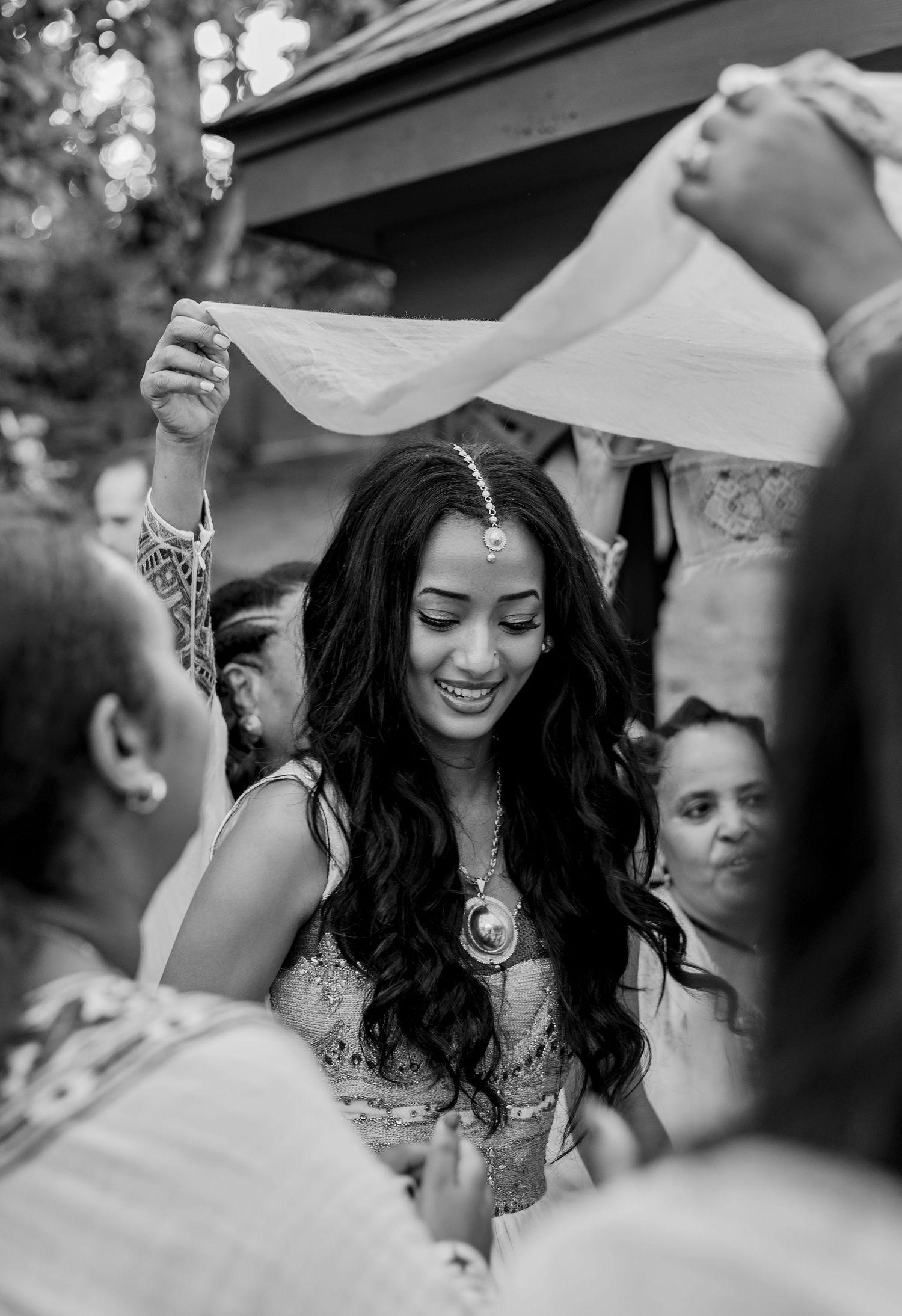 Black and white photo of a smiling Indian bride in traditional jewelry during a wedding ceremony ritual.