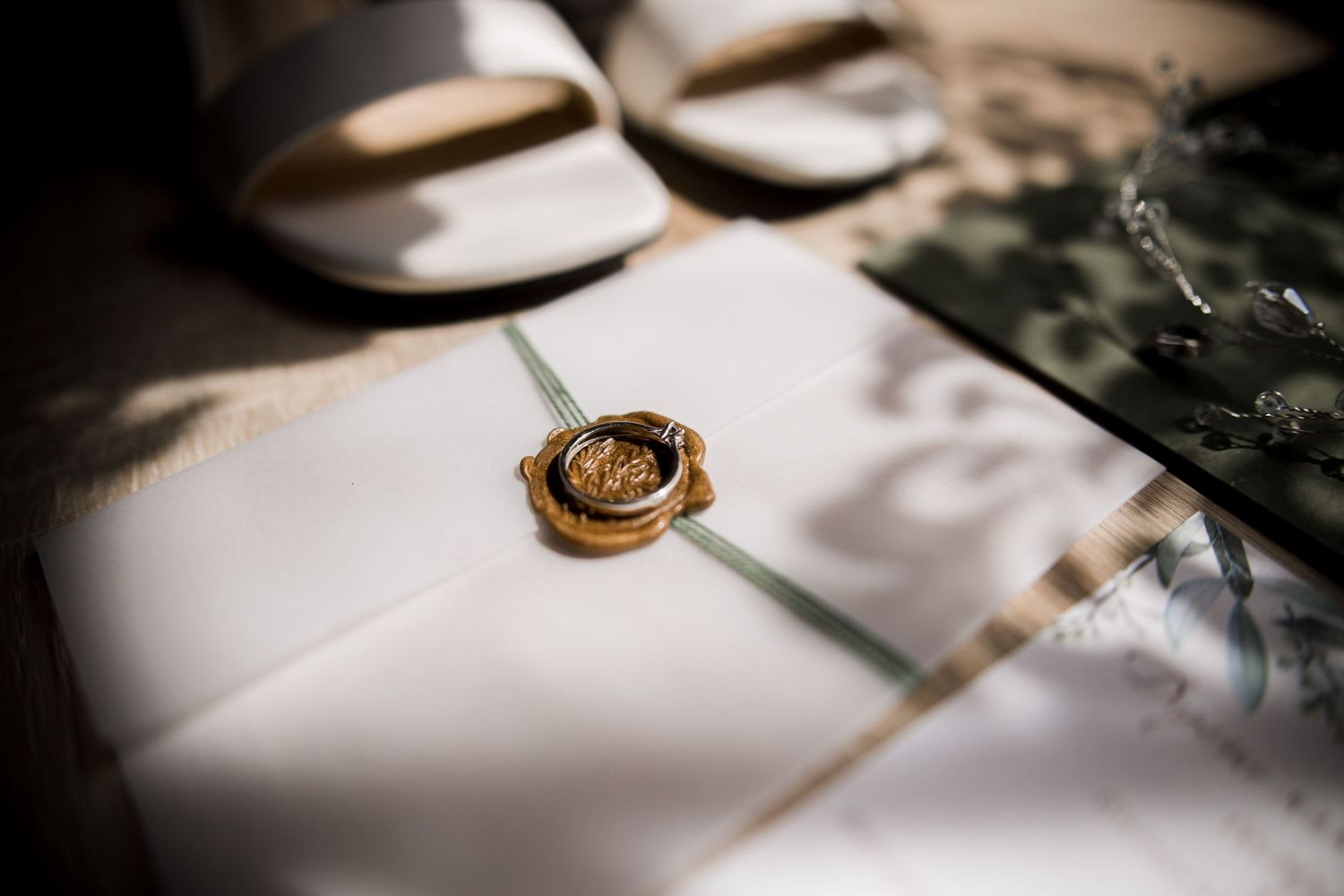 Elegant wedding invitation sealed with a gold wax seal, resting beside white bridal sandals on a marble surface.