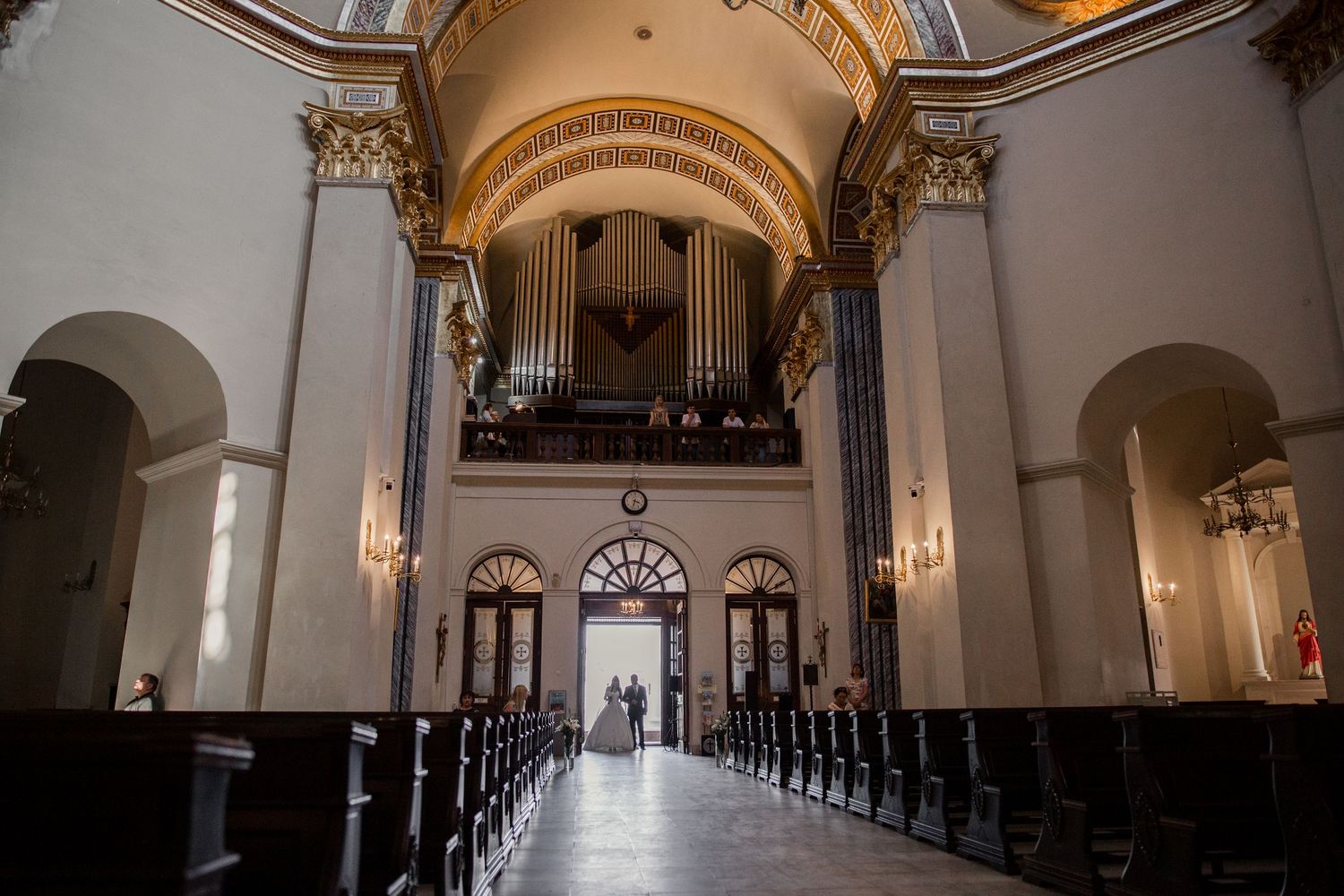 Grand church interior with pipe organ, ornate columns, wooden pews, and arched ceiling in a classic baroque style.