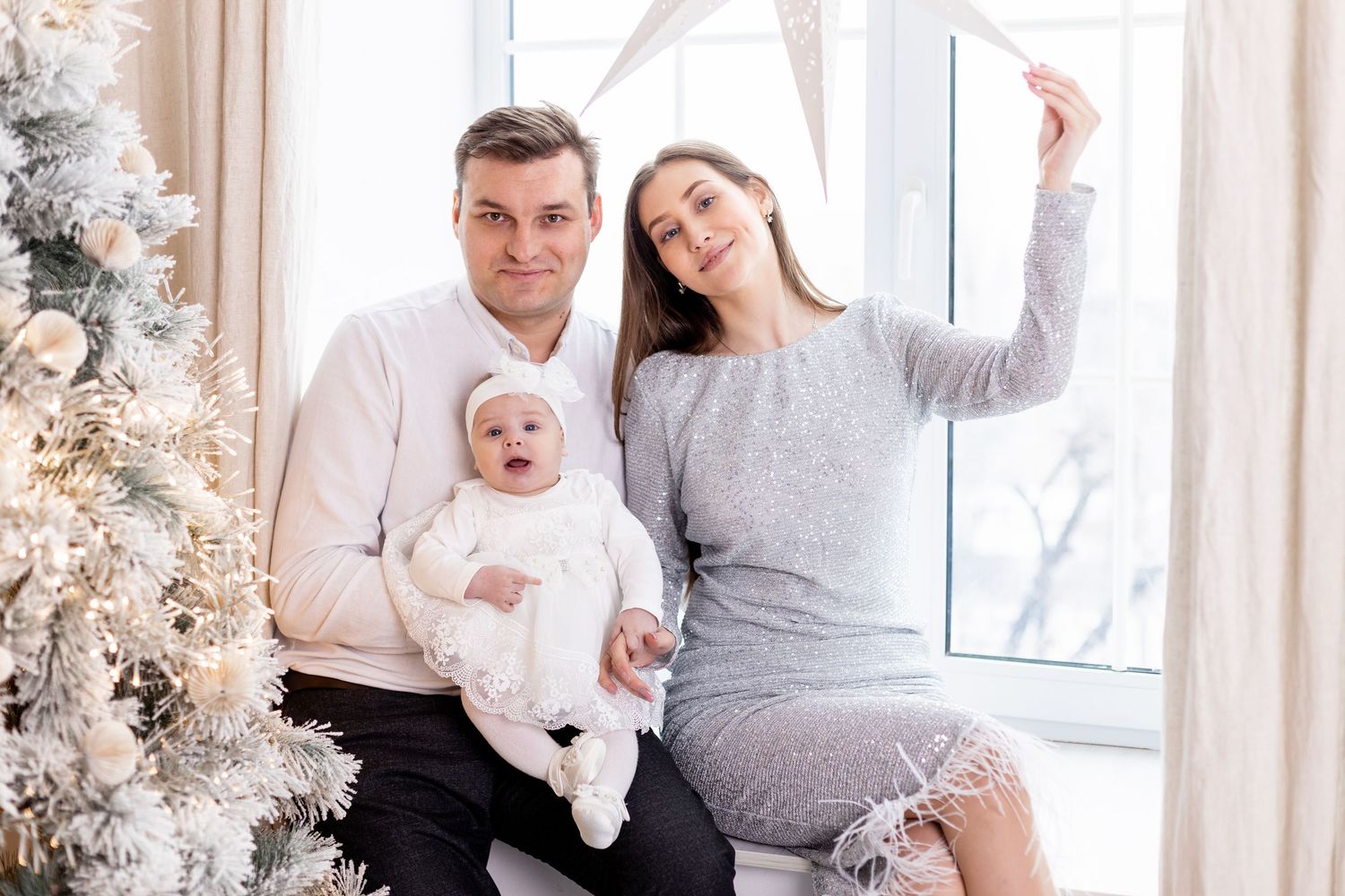 A cozy family Christmas photoshoot with a decorated tree and white decor in the background.