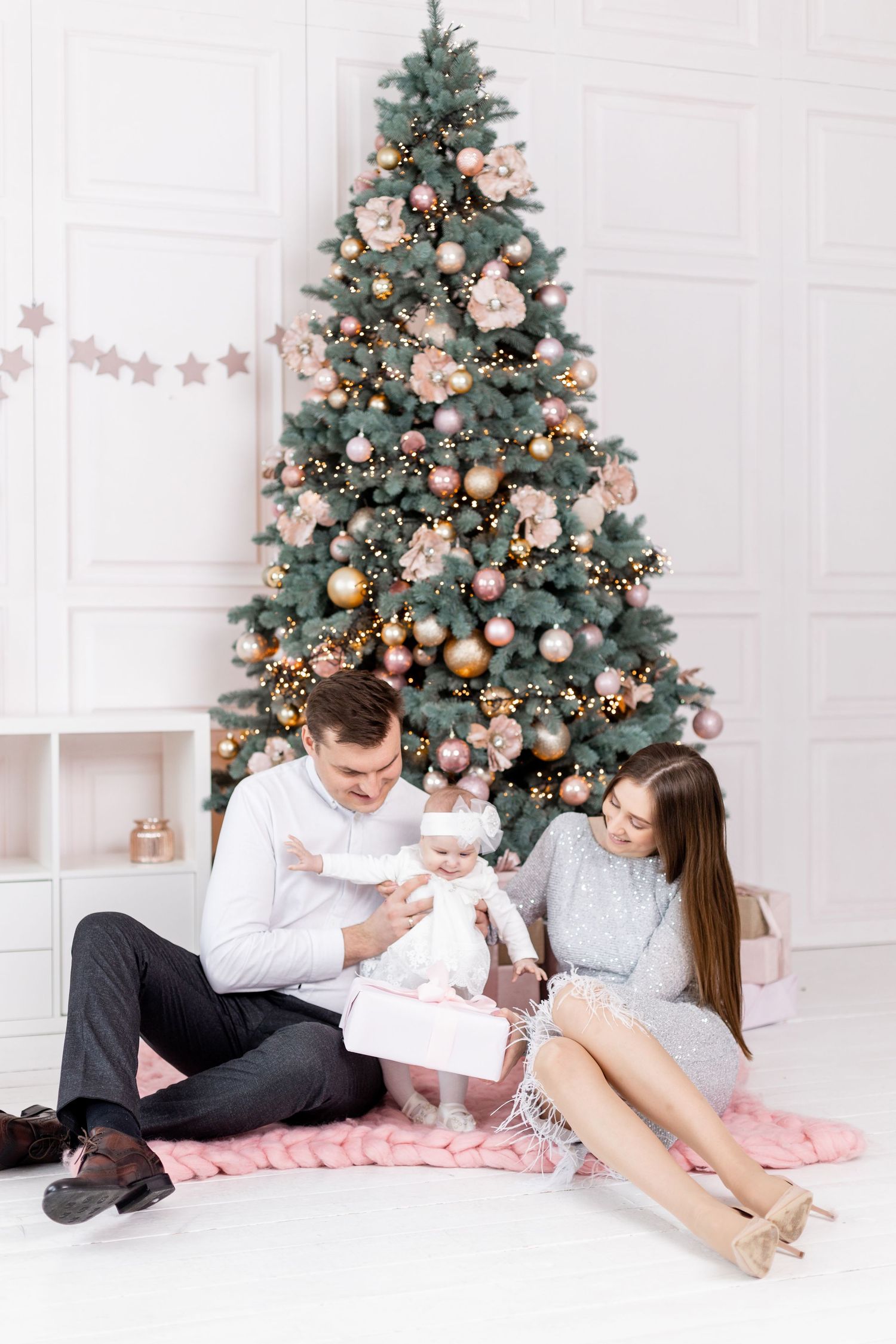 Family relaxing on floor by Christmas tree with wrapped presents.