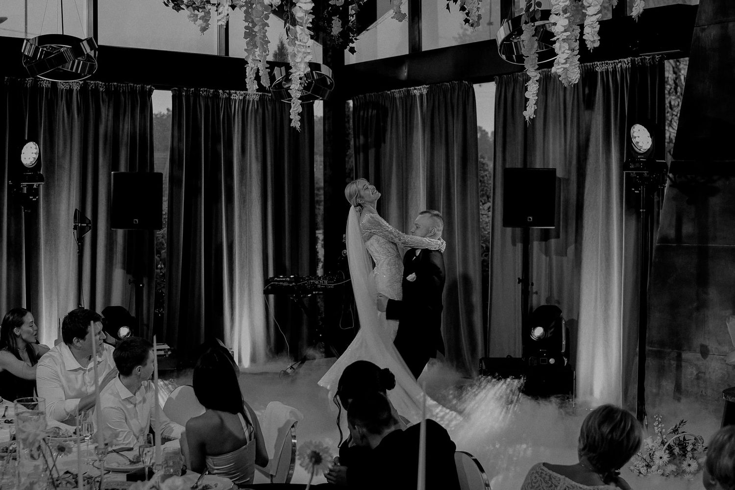 Couple sharing first dance at elegant wedding reception in black and white photo with floral decorations.