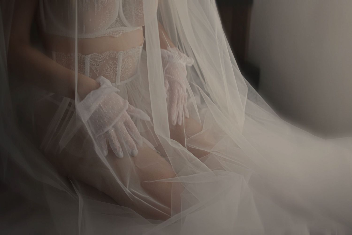 Close-up of a bride in a sheer veil wearing delicate white lace gloves, soft romantic bridal detail photography.