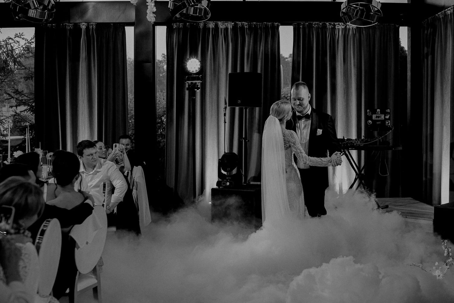 Black and white photo of bride and groom sharing first dance surrounded by fog at elegant wedding reception.
