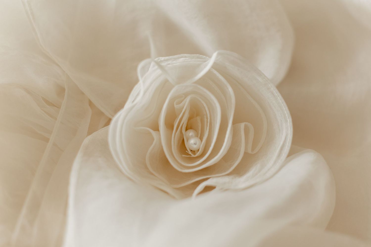 Elegant cream fabric rose with delicate layered petals and a pearl center on soft ivory cloth background.