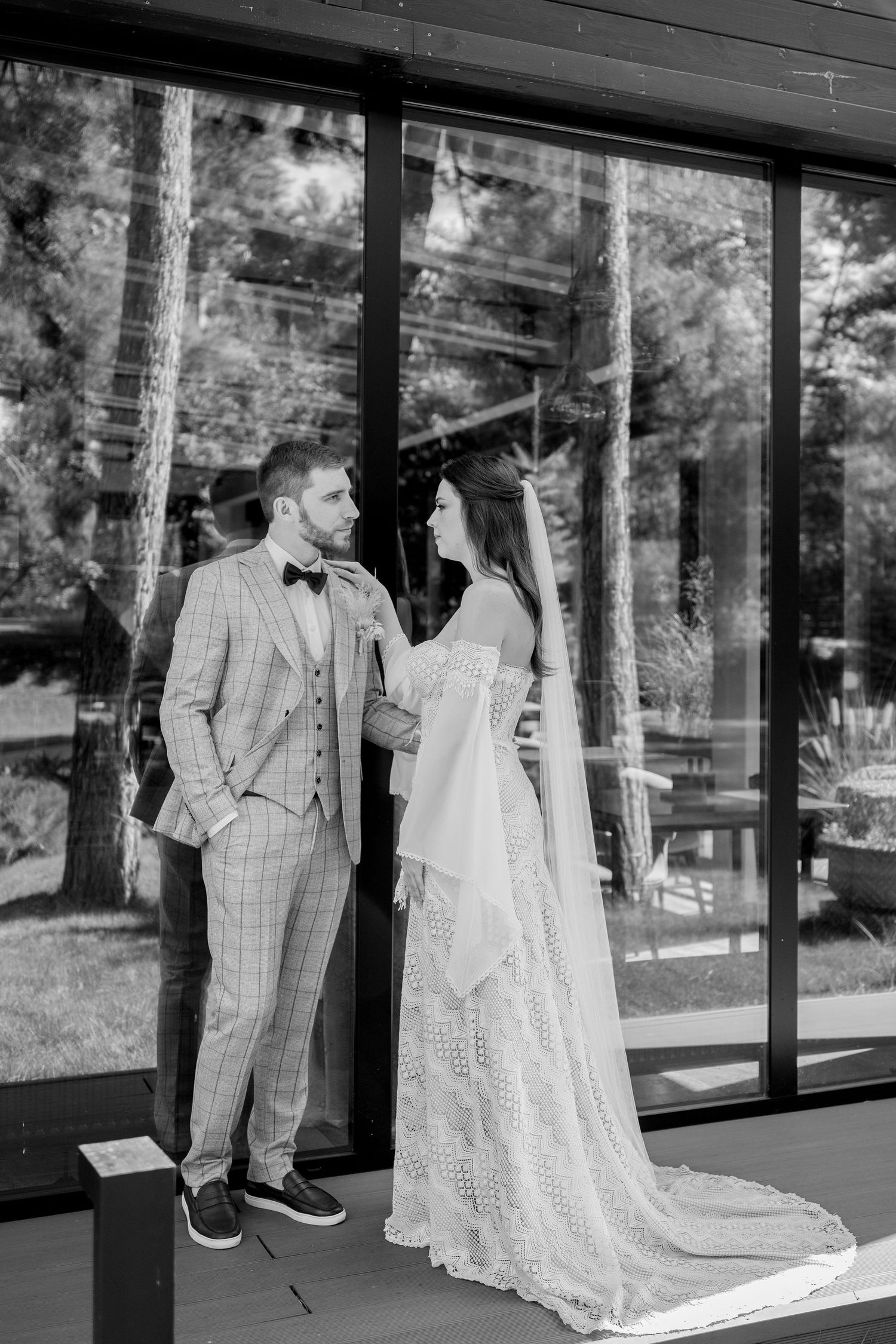Wedding couple embracing by reflective glass windows in a modern architectural setting.