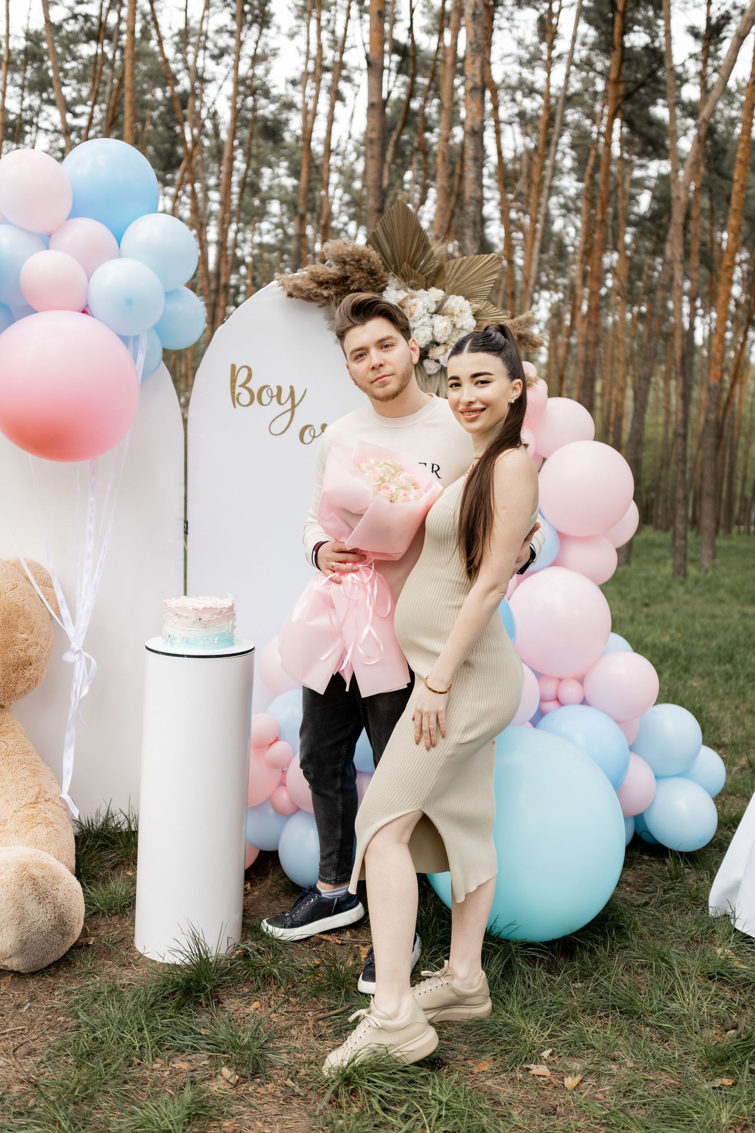Outdoor baby gender reveal party with balloon arch and teddy bear decorations.