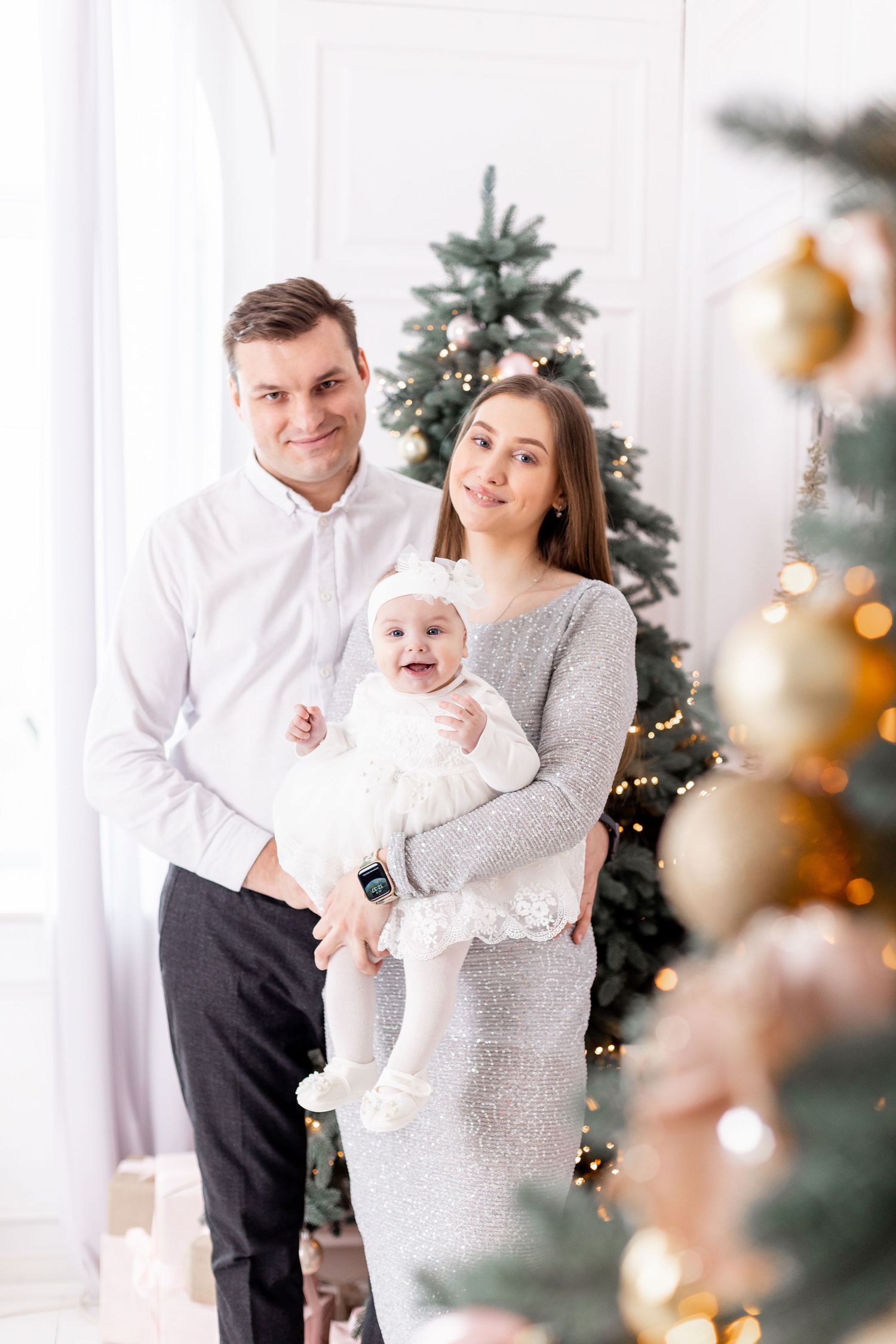 Family in festive attire posing by Christmas tree with rose gold ornaments.