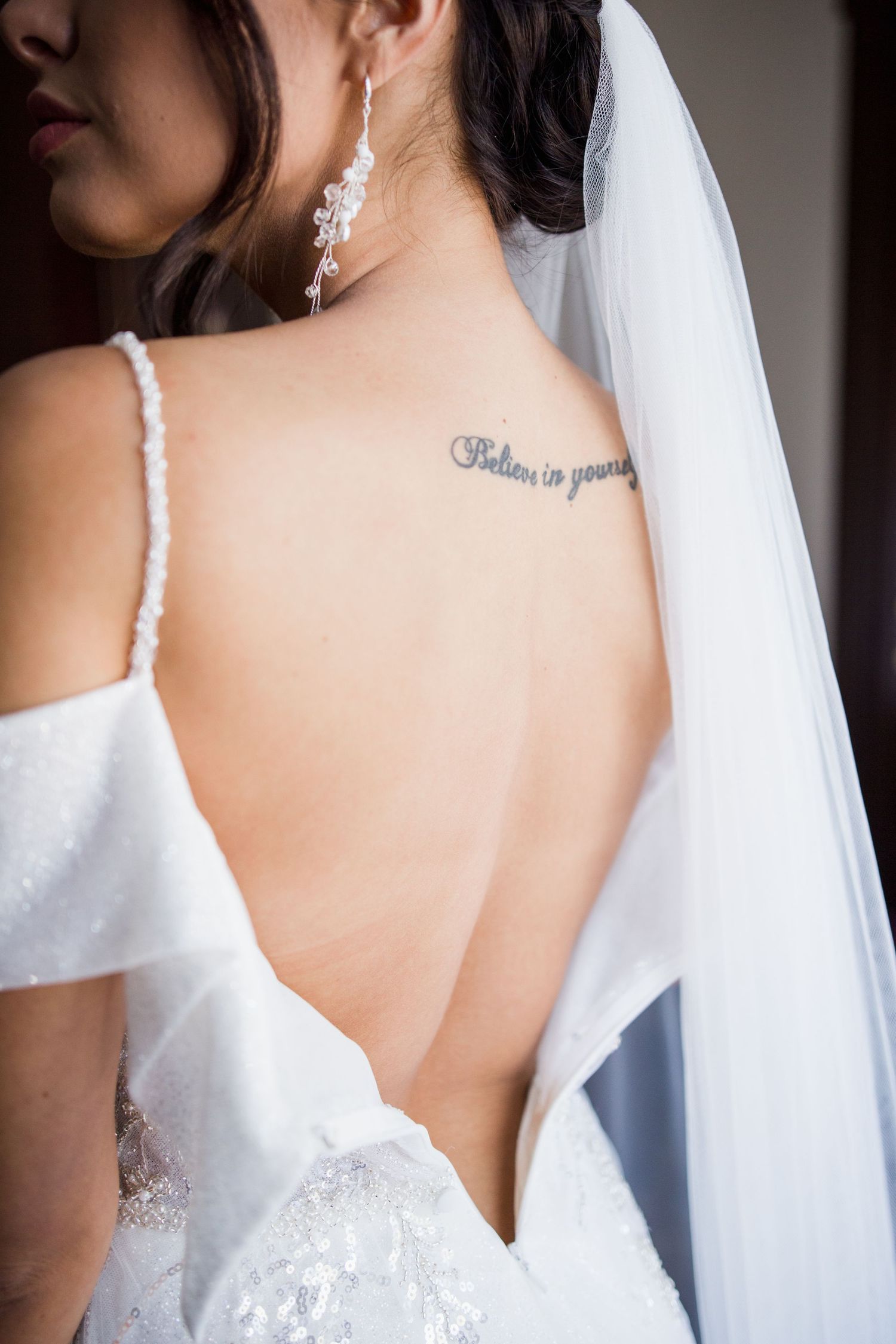 Bride in backless white wedding gown and veil with believe in yourself tattoo on her upper back.