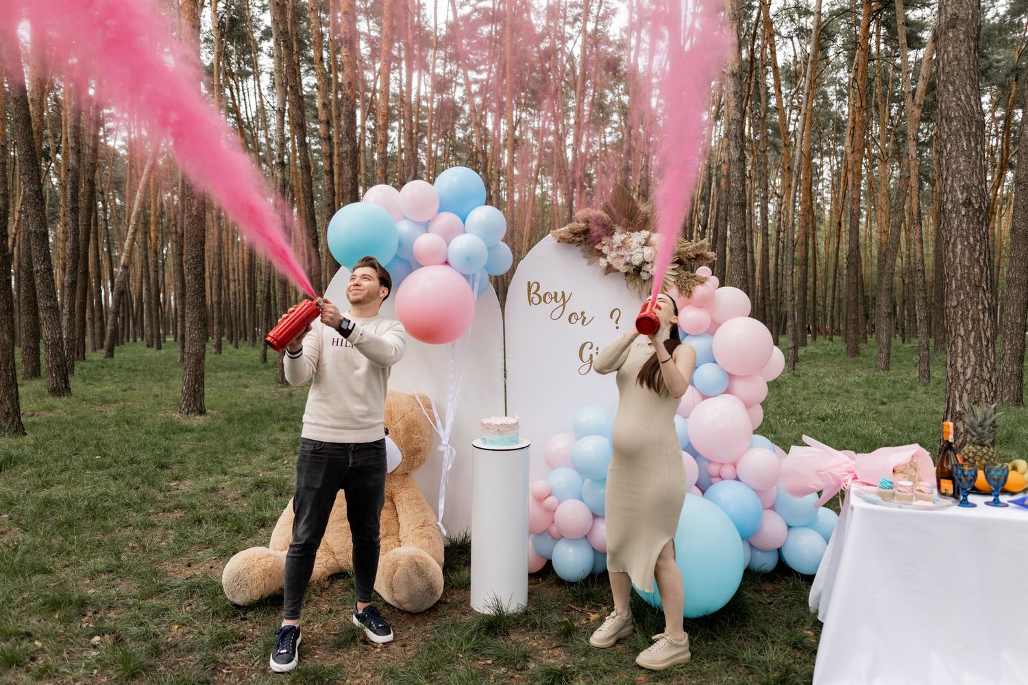 Gender reveal celebration with pink smoke effects and festive balloon arrangements in forest.
