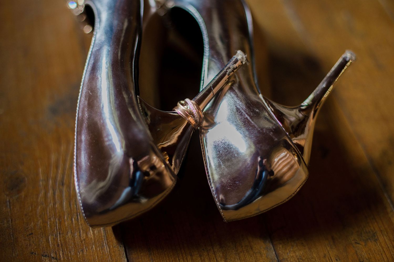 Close-up of elegant metallic bronze high heel shoes with bow detail on wooden floor.
