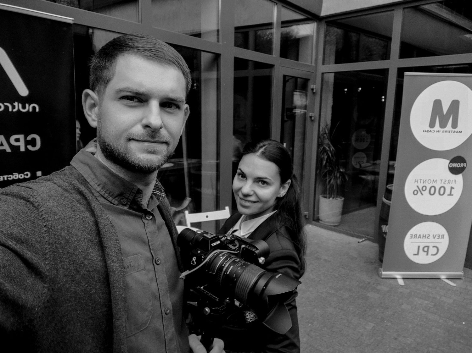 Man and woman taking a selfie with a camera at an outdoor event, black and white photography.