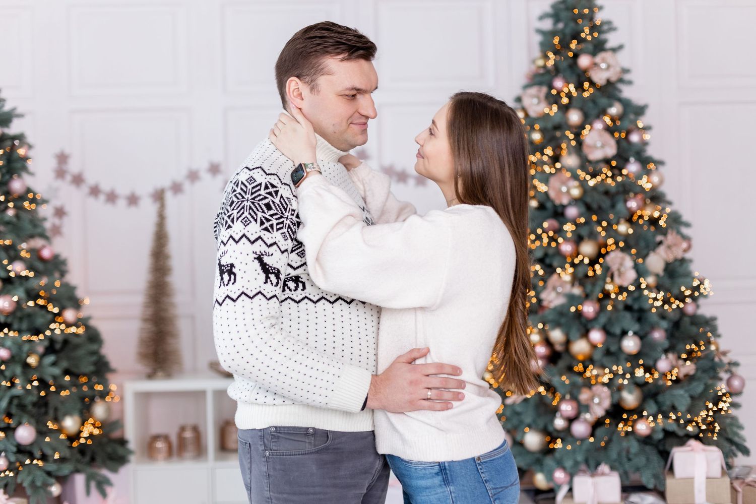 Holiday photoshoot scene with decorated Christmas trees and romantic moment.