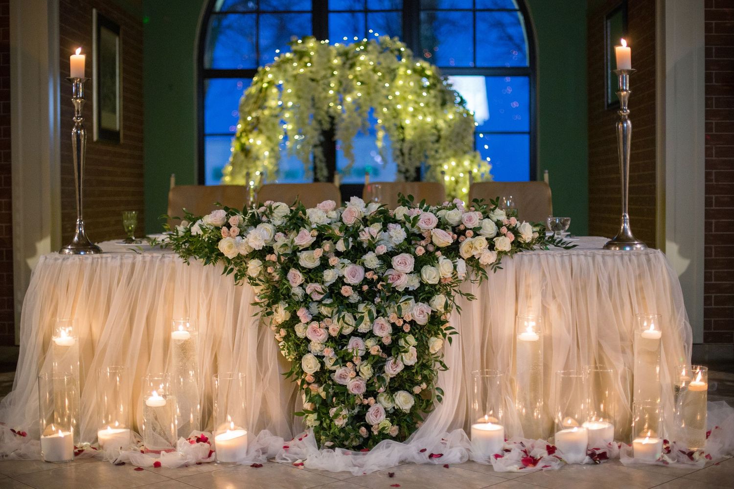 Elegant wedding sweetheart table adorned with pink roses, candles, tulle, and a glowing floral tree centerpiece.
