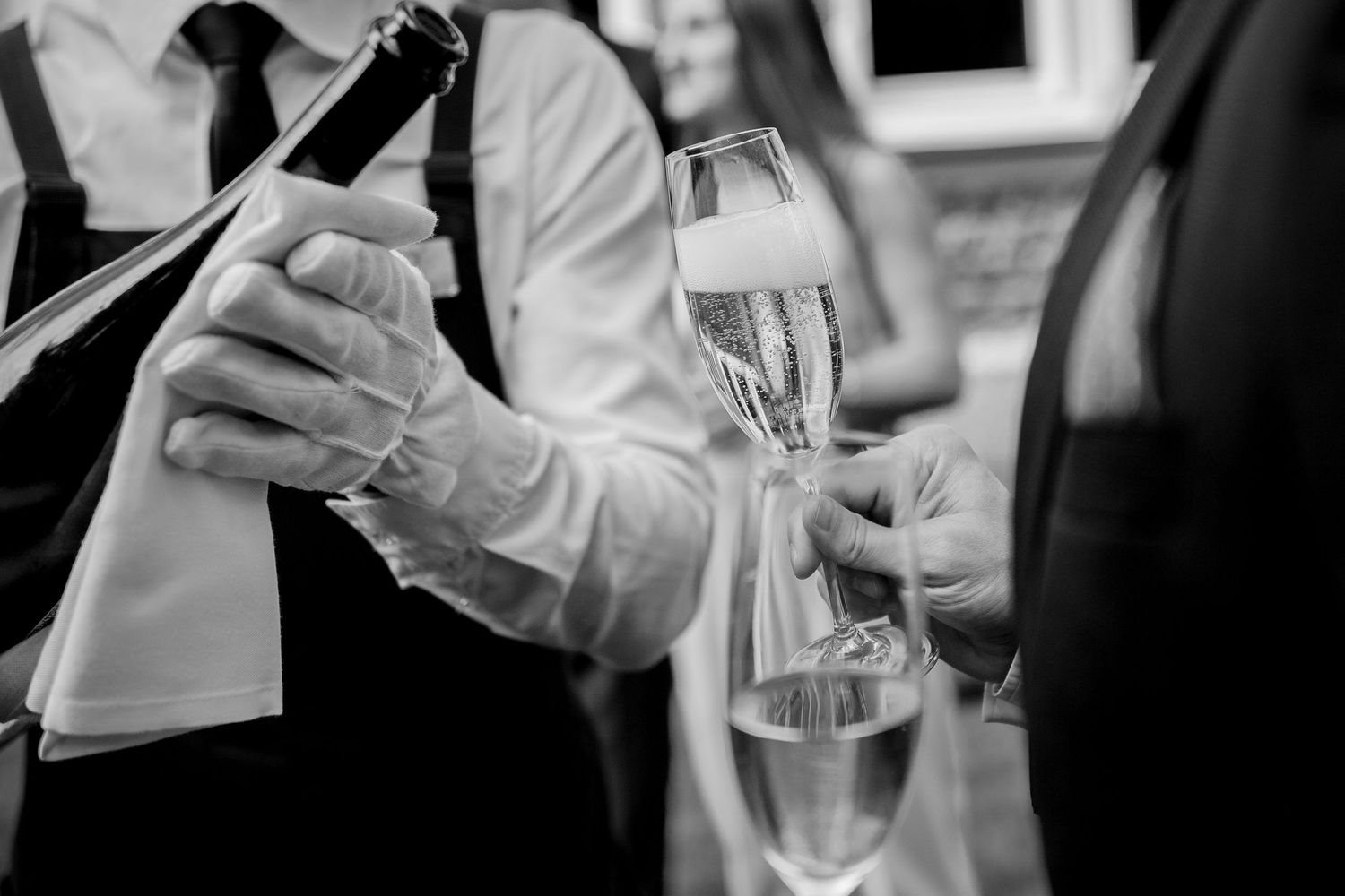 Black and white photo of a waiter pouring champagne into flutes at a formal event.
