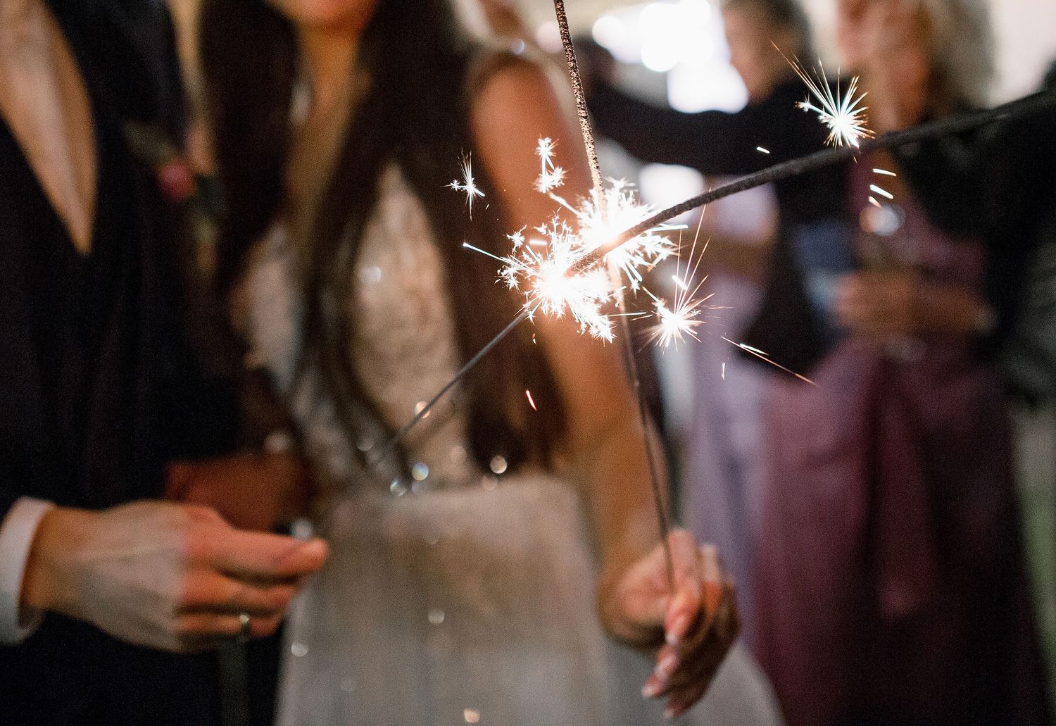 Guests holding sparklers at a wedding celebration with bride in background.