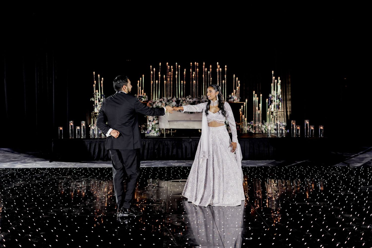Couple sharing first dance on starlit floor with elegant candlelit backdrop at a luxurious wedding reception.
