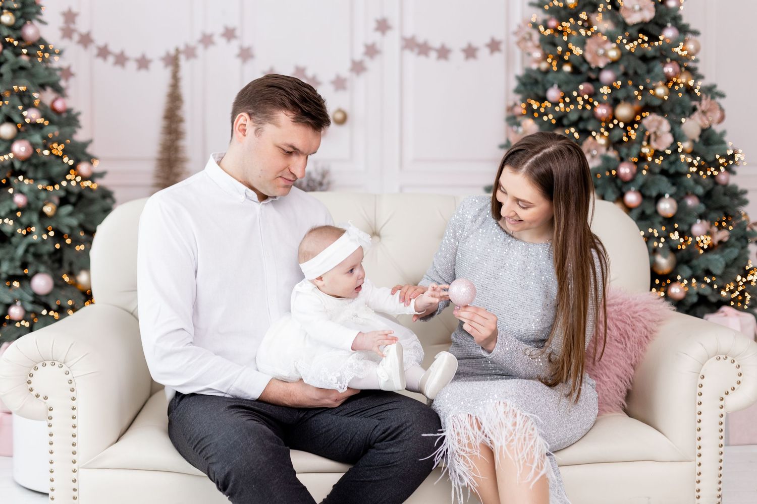Family posing by decorated Christmas tree in white and grey outfits.