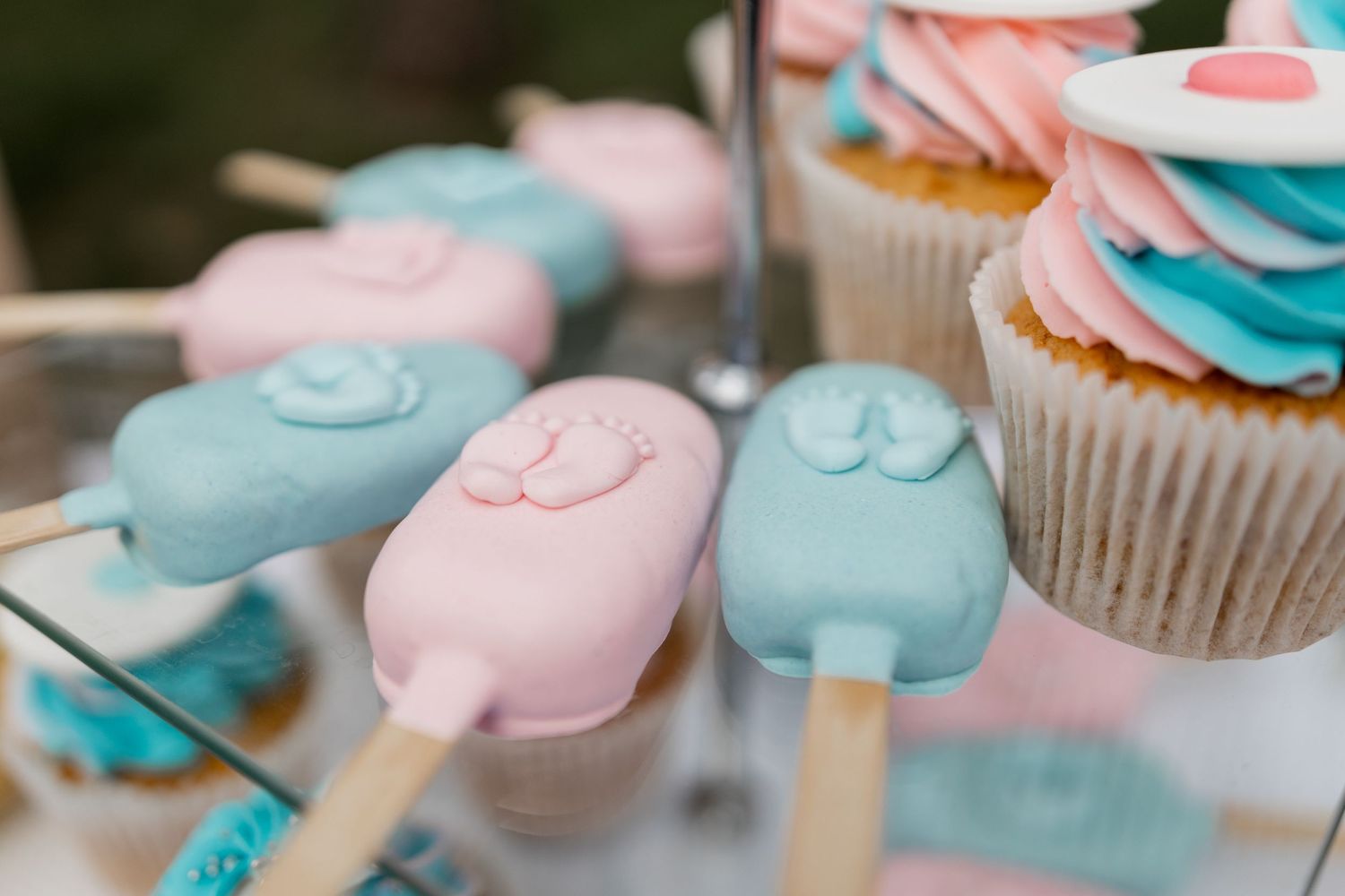 Close-up of pink and blue popsicle-shaped cookies and cupcakes on a dessert stand.