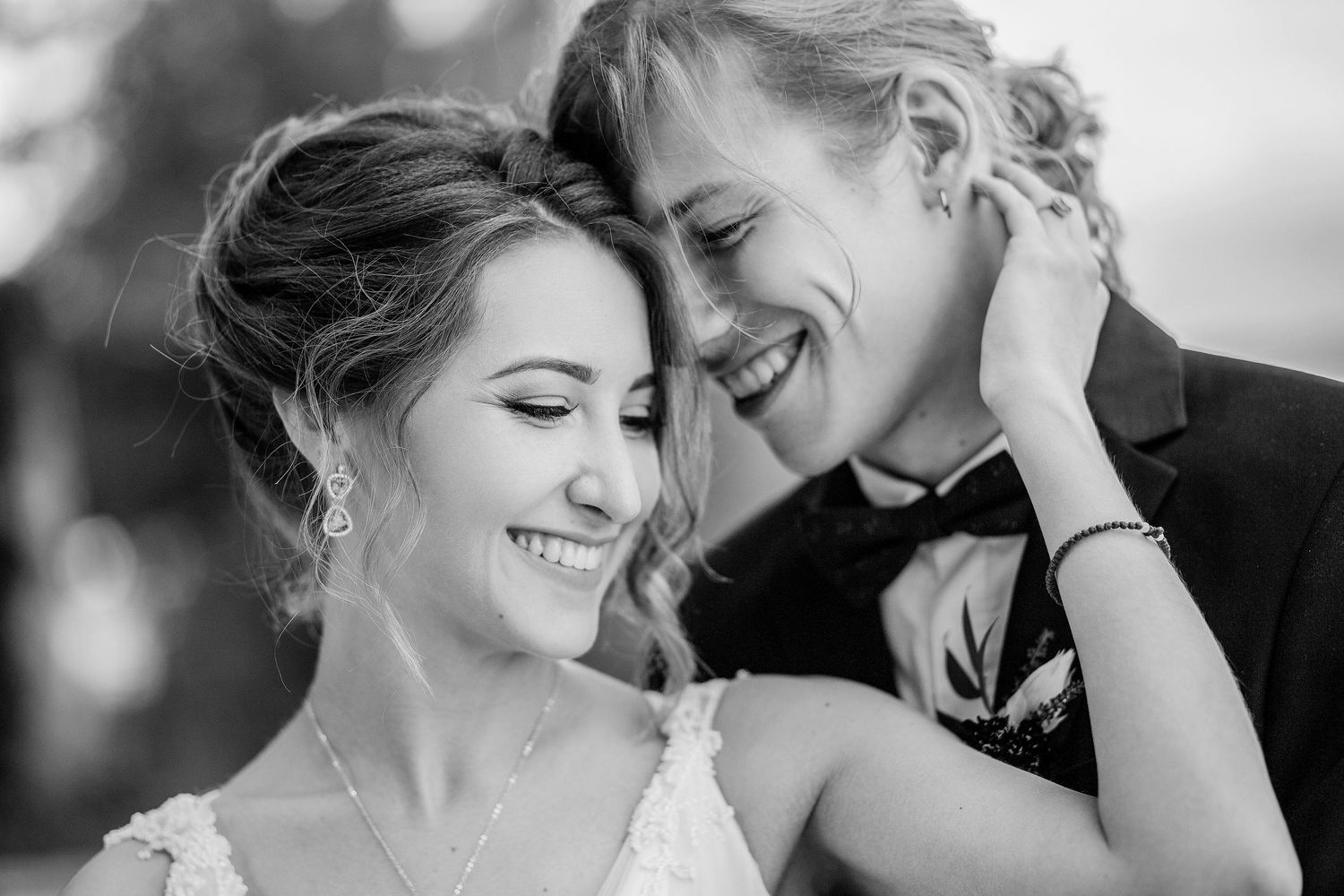 Black and white wedding photo of smiling bride and groom sharing an intimate moment, bride in lace gown with pearl jewelry.