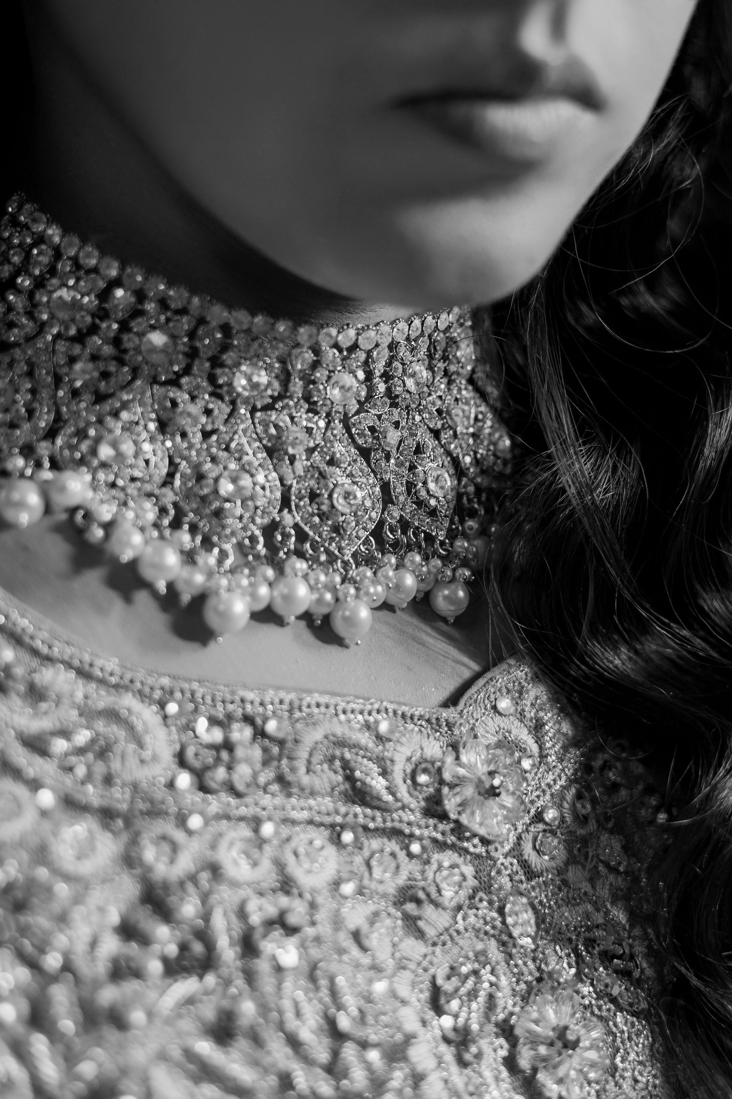 Black and white close-up of a bride wearing an ornate beaded necklace and heavily embroidered bridal outfit.