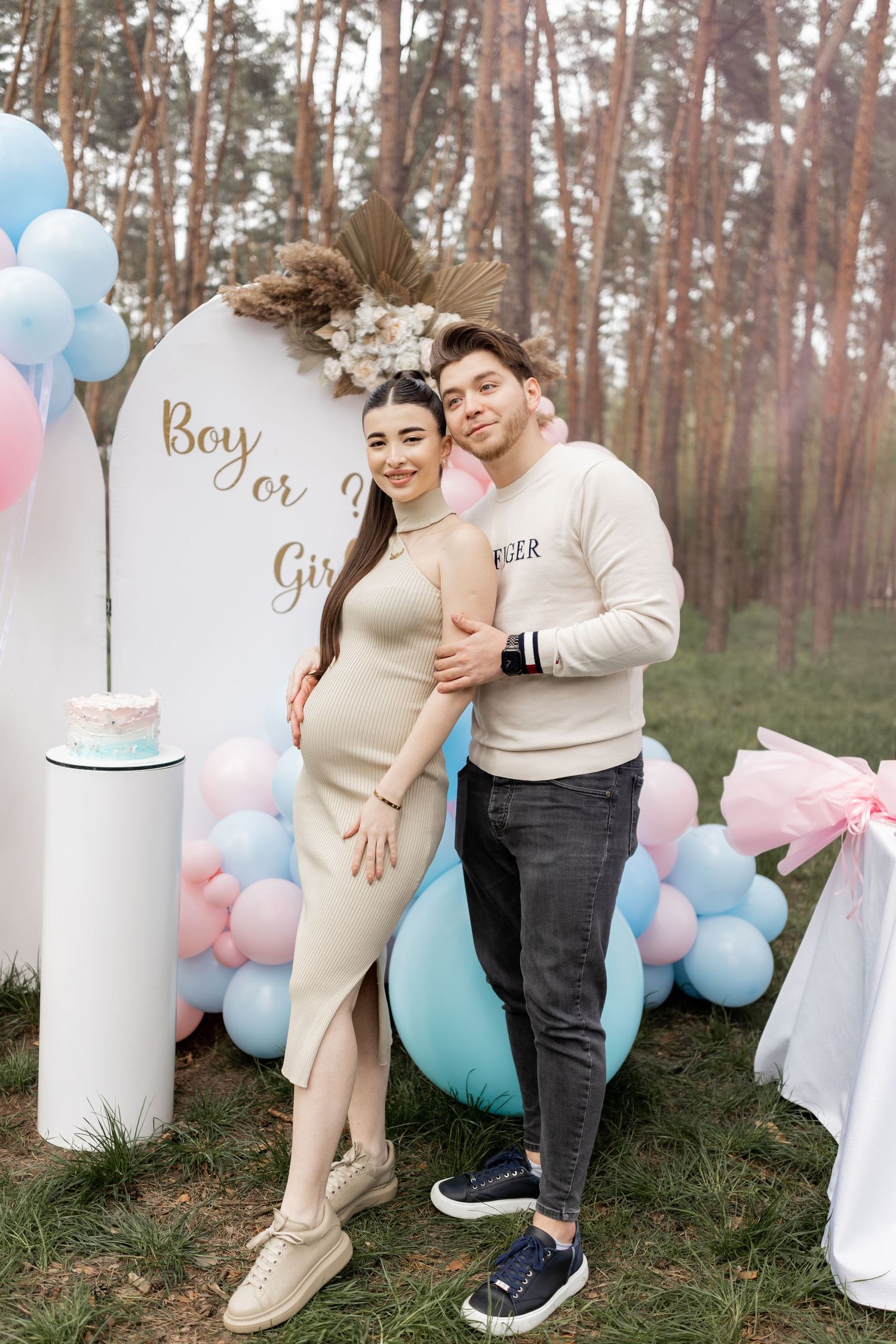 Outdoor gender reveal celebration with pastel balloon arch and decorative white columns.