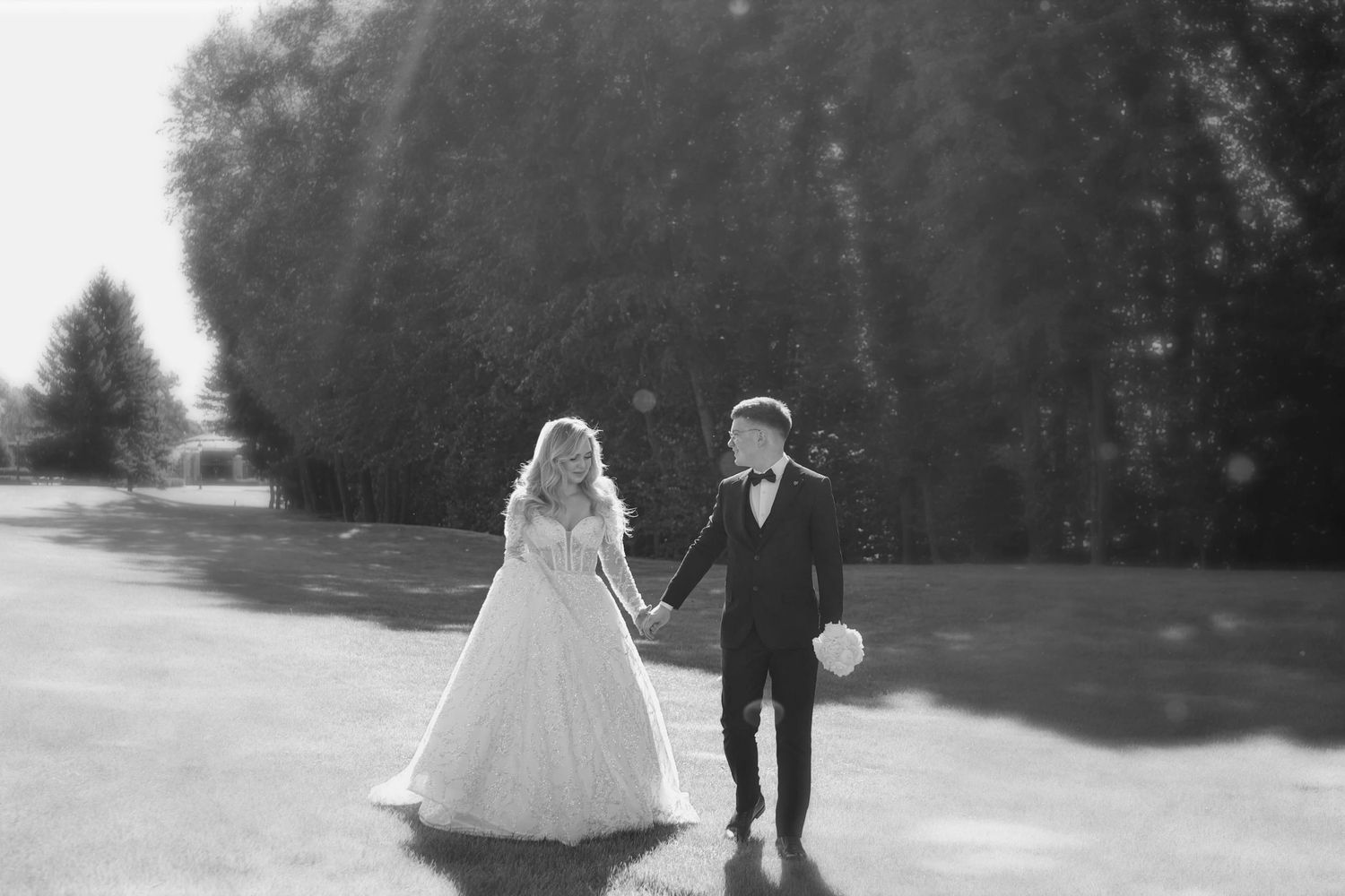 Black and white photo of a bride and groom holding hands outdoors on their wedding day.