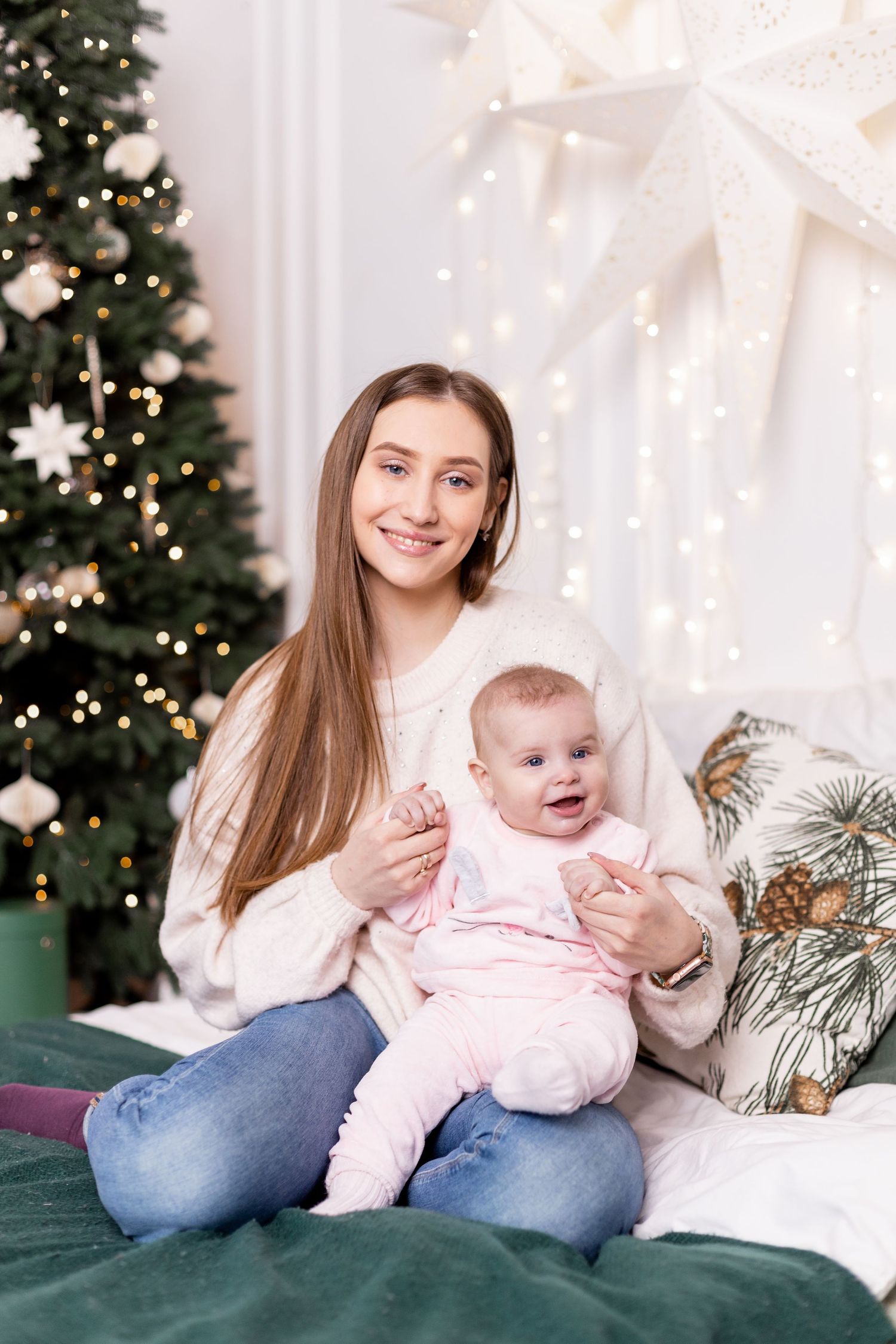 Holiday family photoshoot with baby in pink outfit against Christmas decorations.