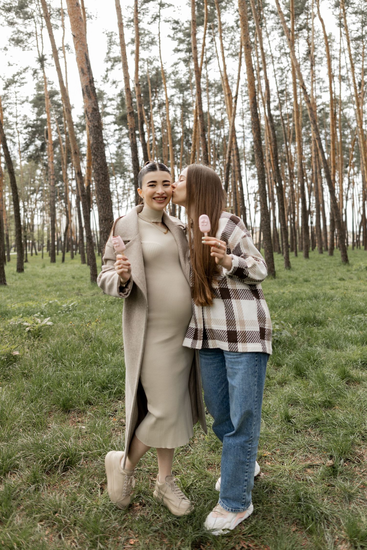 Two people enjoy ice cream treats while posing in a pine forest.